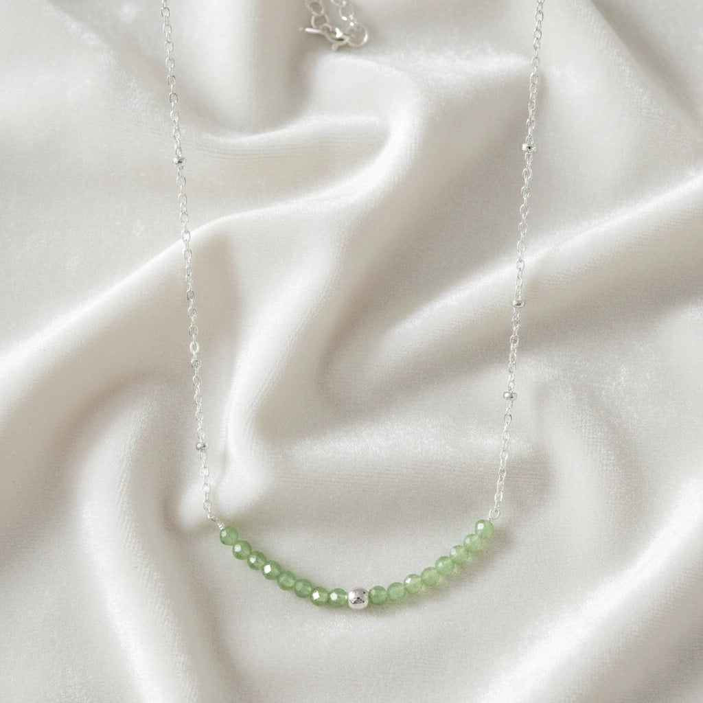 Peridot_necklace_in_sterling_silver_with_peridot_stones_in_beaded_design_in_zoomed_view_on_a_white_fabric_background