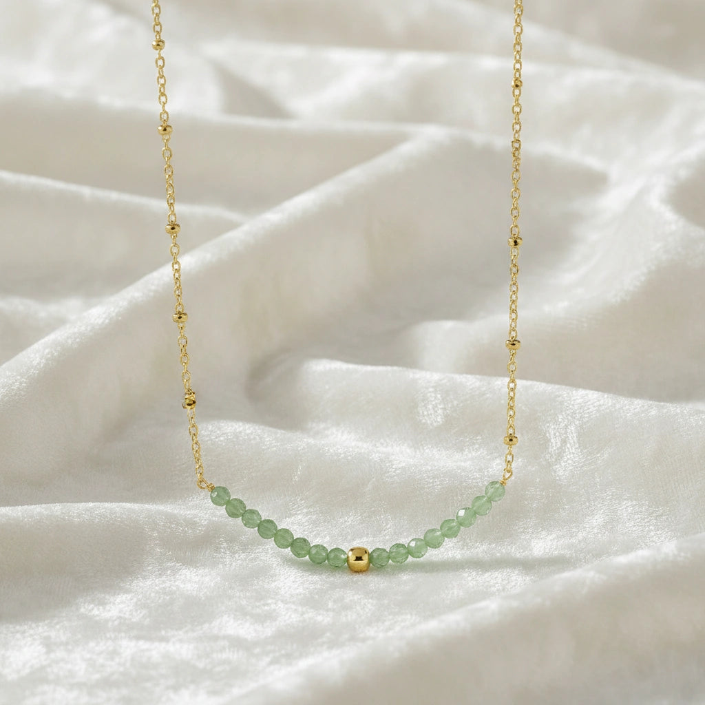Peridot_necklace_in_gold_plated_silver_with_peridot_stones_in_beaded_design_in_zoomed_view_on_a_white_fabric_background