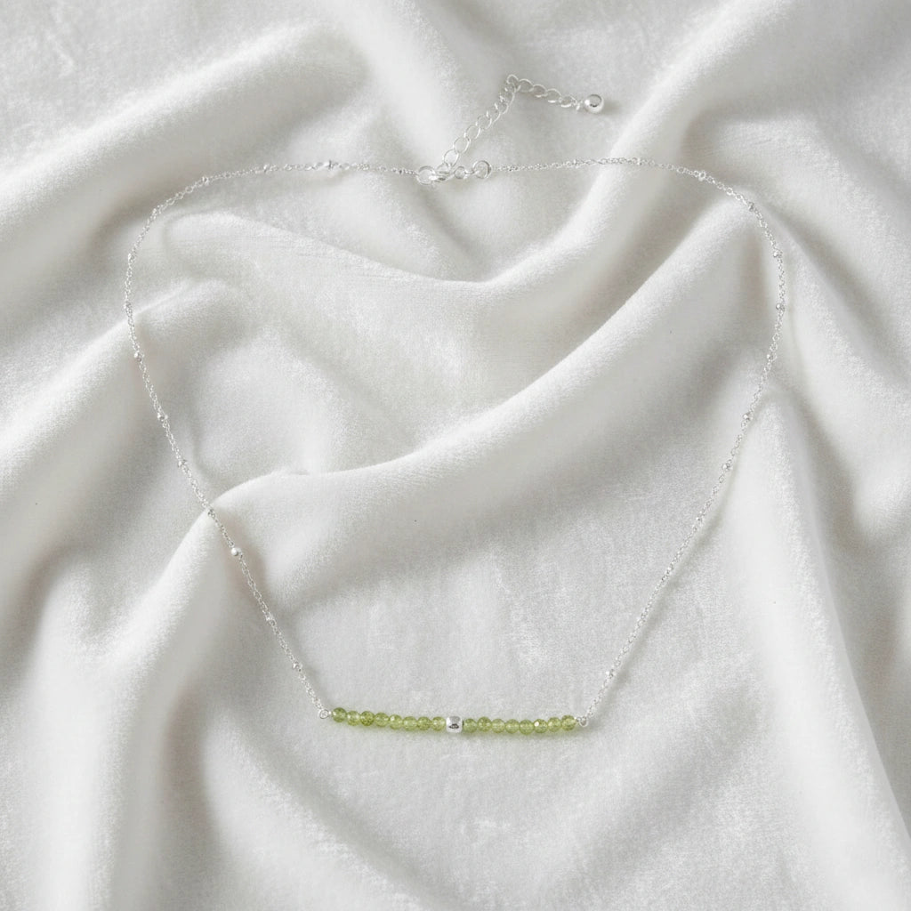 Peridot_necklace_in_sterling_silver_with_peridot_stones_in_beaded_design_in_front_angle_on_a_white_fabric_background