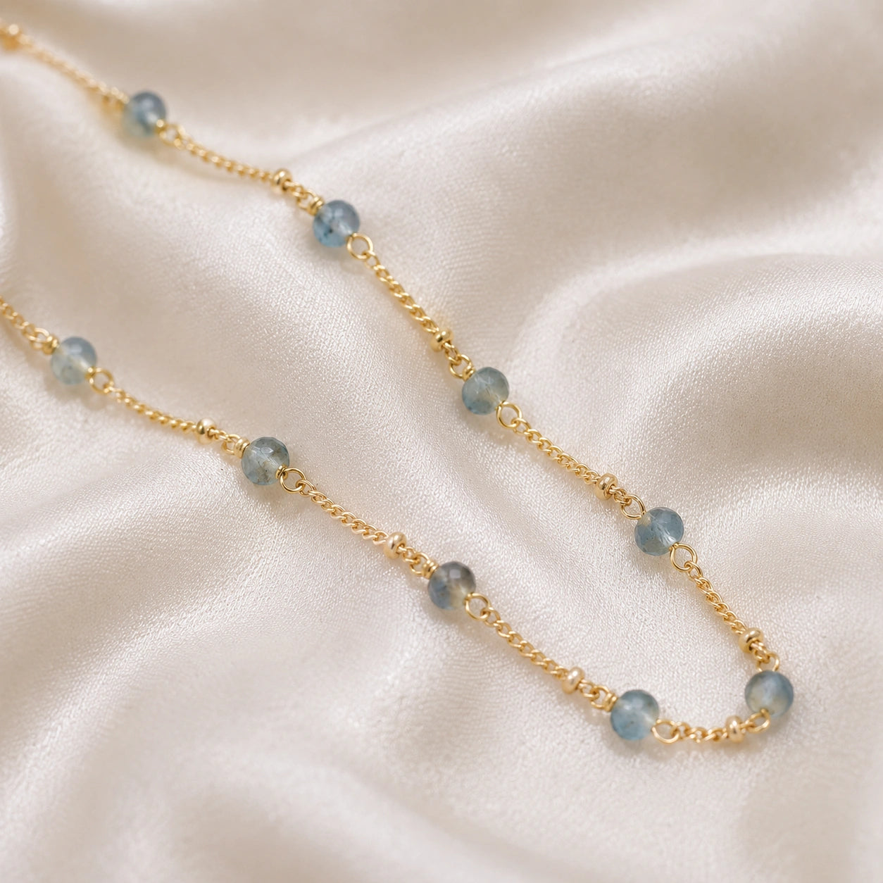 Beads_necklace_in_gold_plated_silver_at_slight_angle_with_aquamarine_stones_on_a_soft_fabric_background