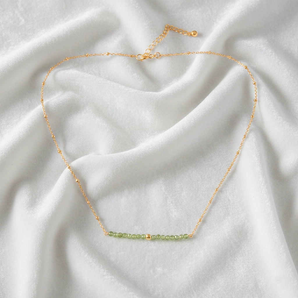 Peridot_necklace_in_gold_plated_silver_with_peridot_stones_in_beaded_design_in_front_angle_on_a_white_fabric_background