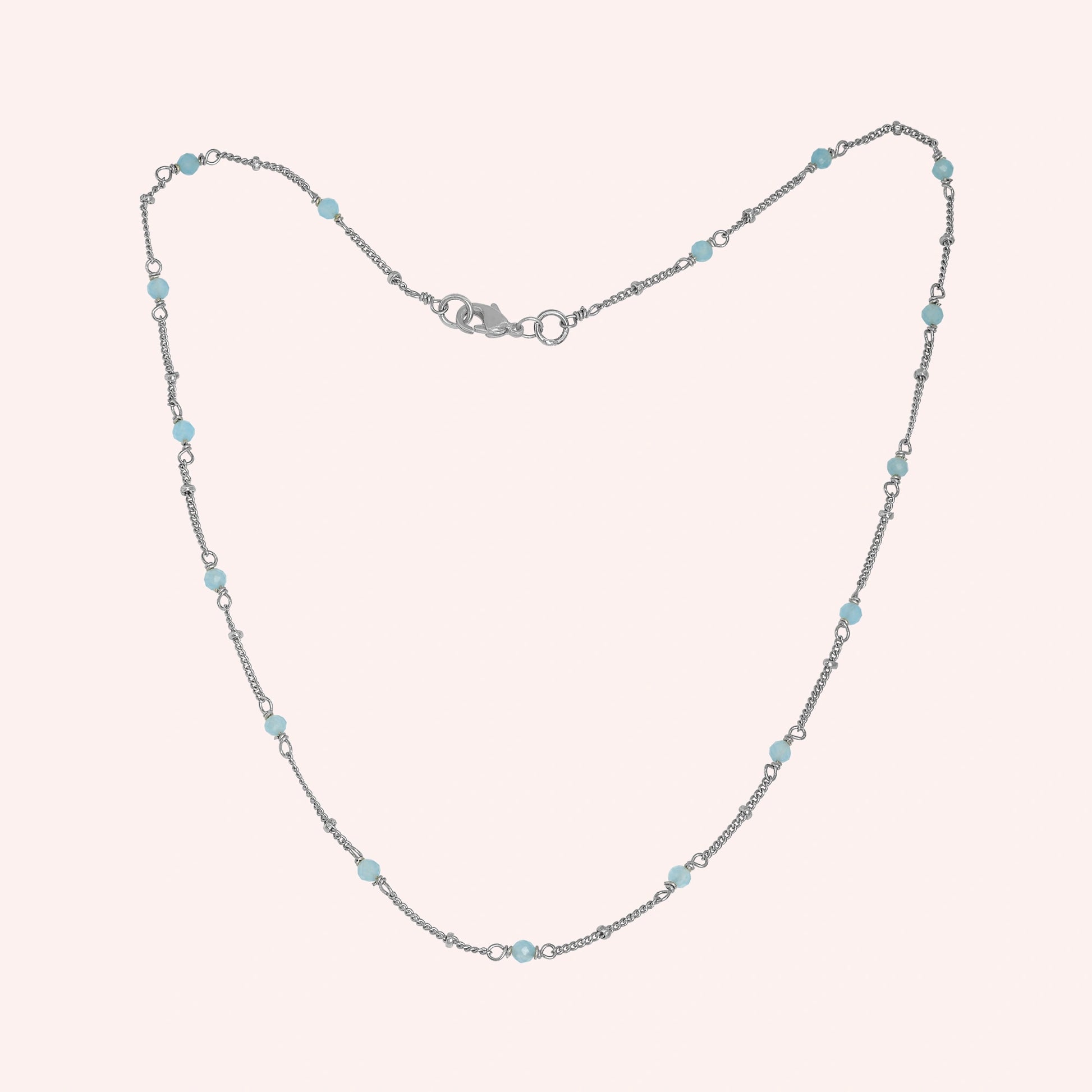Beads_necklace_in_sterling_silver_at_front_angle_with_aquamarine_stones_on_a_solid_pink_background