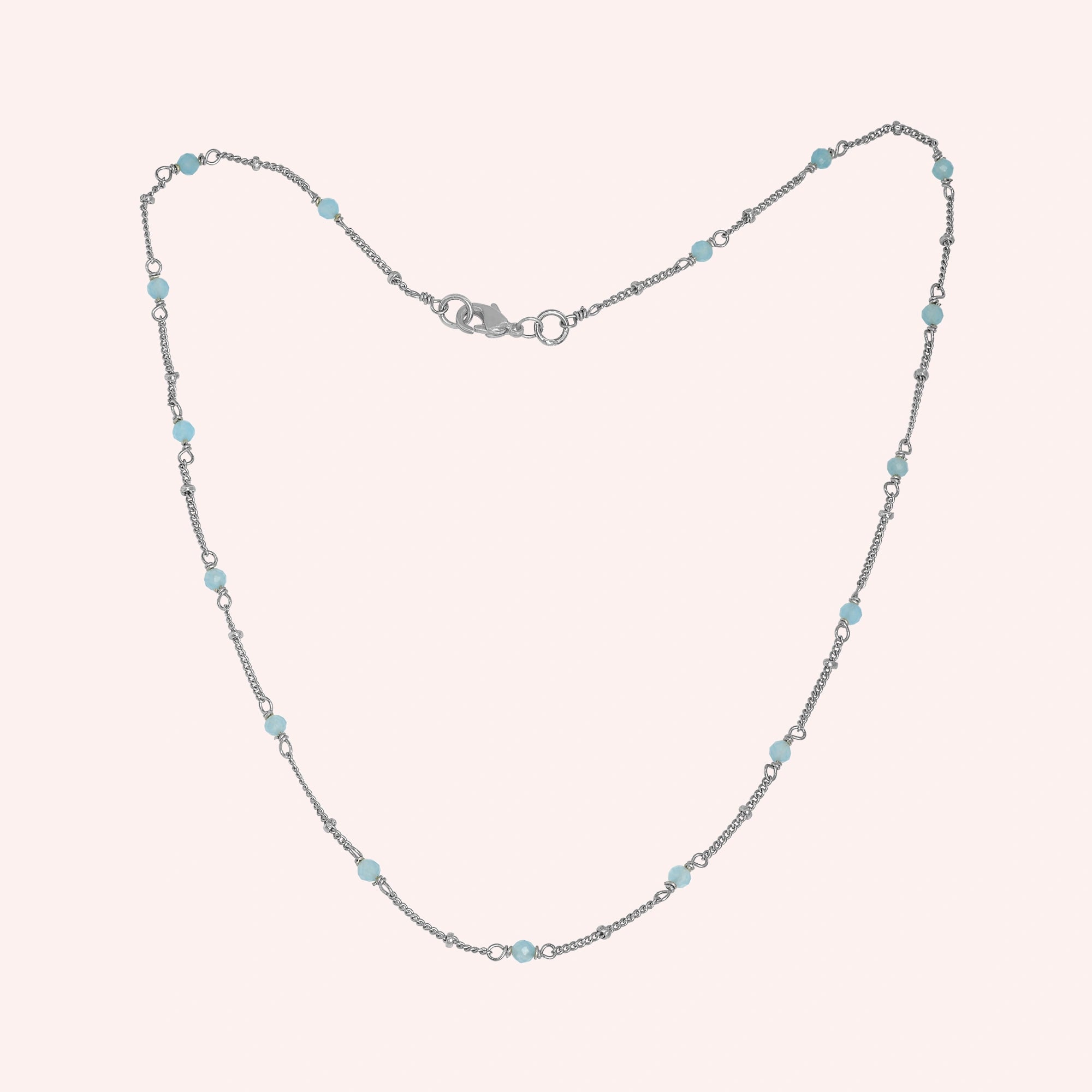 Beads_necklace_in_sterling_silver_at_front_angle_with_aquamarine_stones_on_a_solid_pink_background