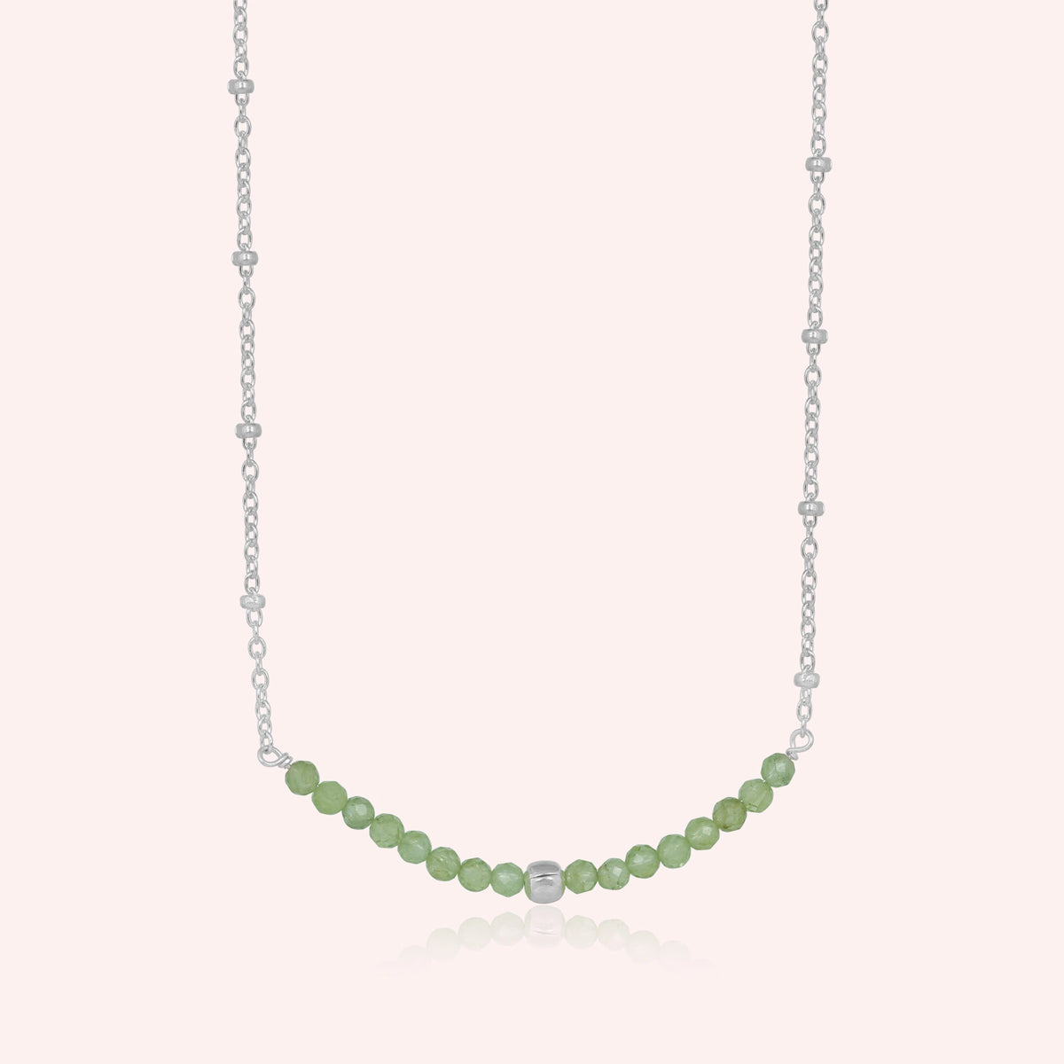 Peridot_necklace_in_sterling_silver_with_peridot_stones_in_beaded_design_in_front_angle_on_solid_pink_background