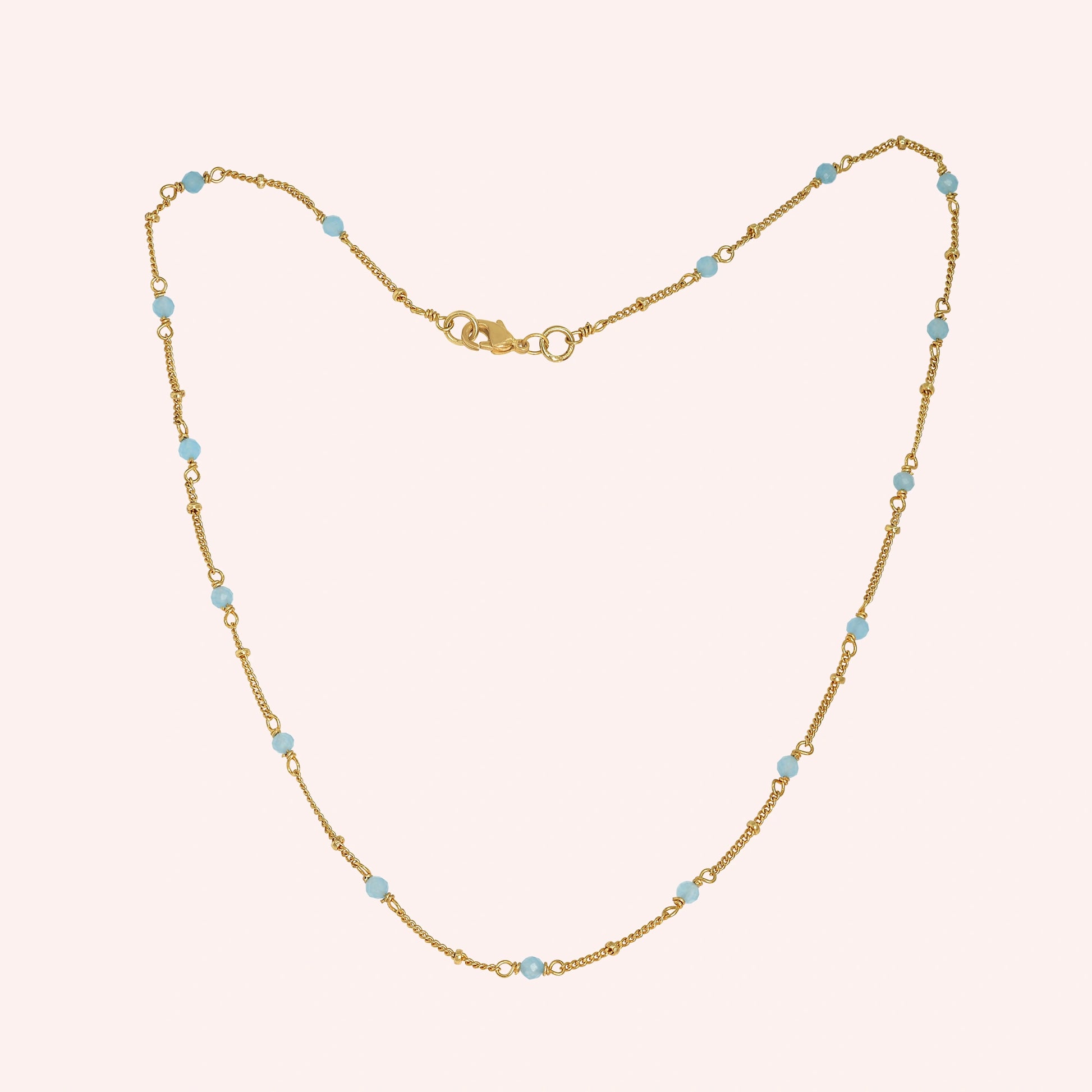 Beads_necklace_in_gold_plated_silver_at_front_angle_with_aquamarine_stones_on_a_solid_pink_background