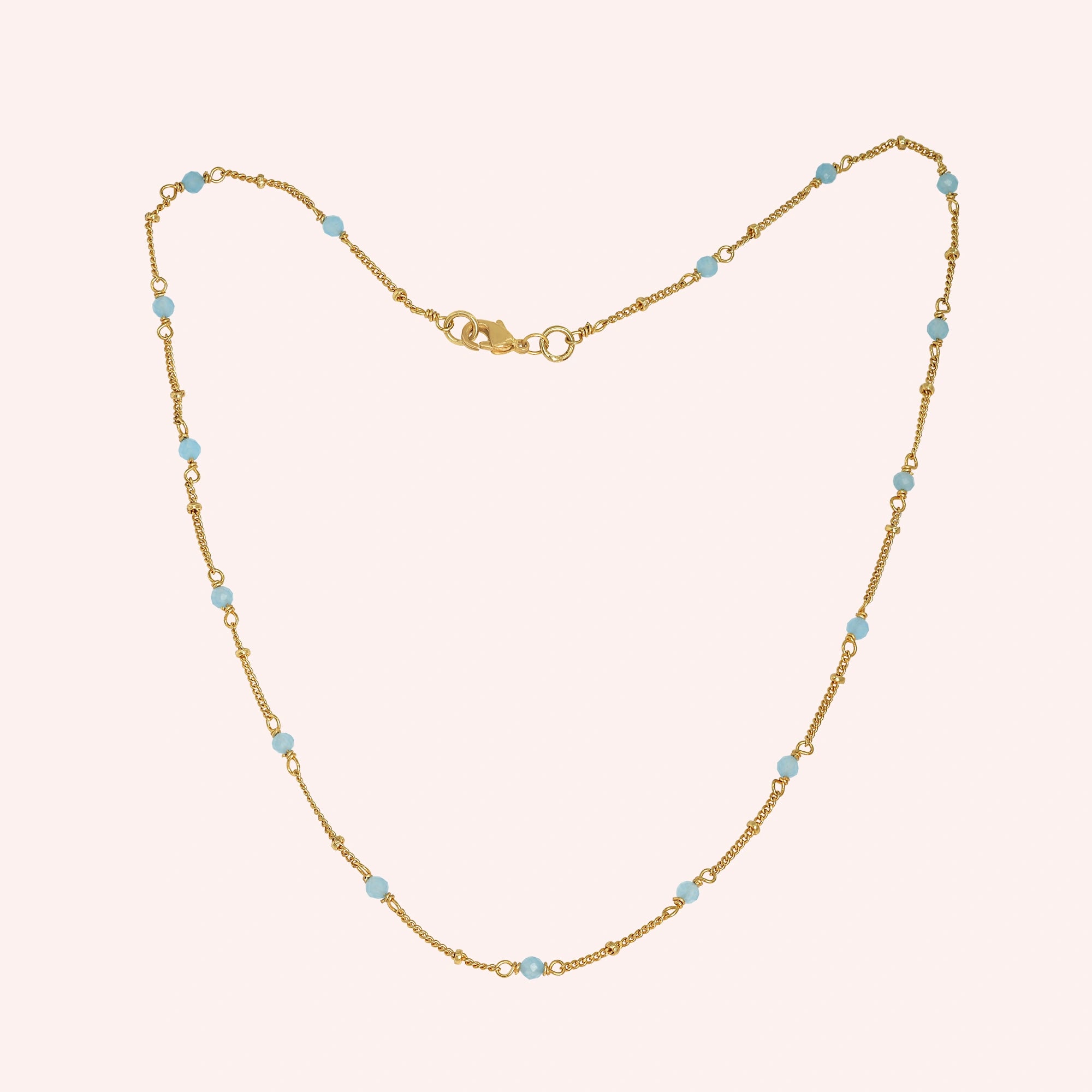 Beads_necklace_in_gold_plated_silver_at_front_angle_with_aquamarine_stones_on_a_solid_pink_background