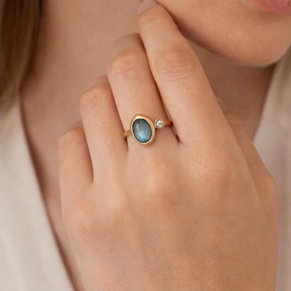 Bezel-set-ring-with-labradorite-and-white-topaz-stone-worn-on-a-model-hand-in-a-natural-light