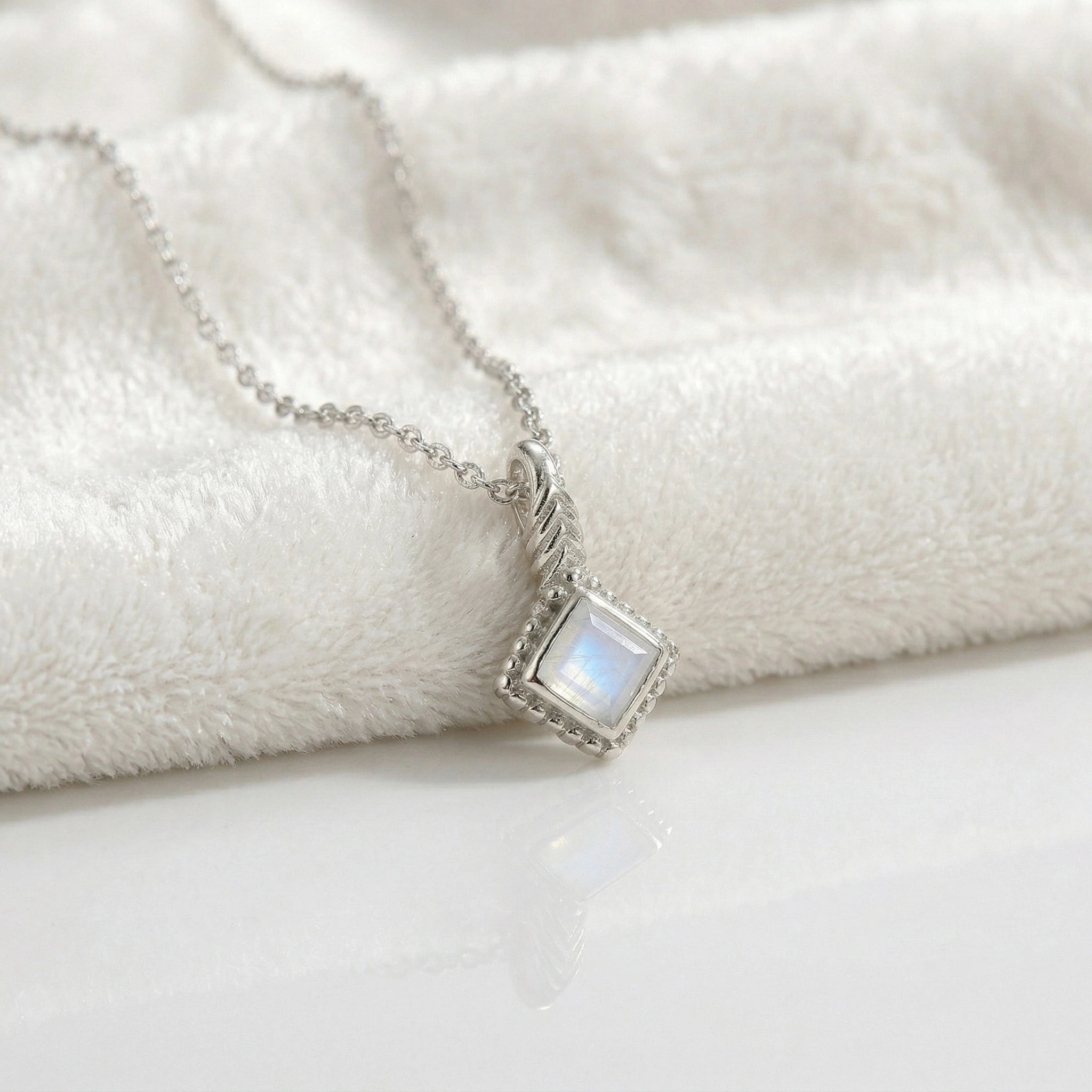 Birthstone_necklace_in_sterling_silver_with_square_cut_moonstone_pendant_in_slightly_angled_view_on_soft_white_fabric_background