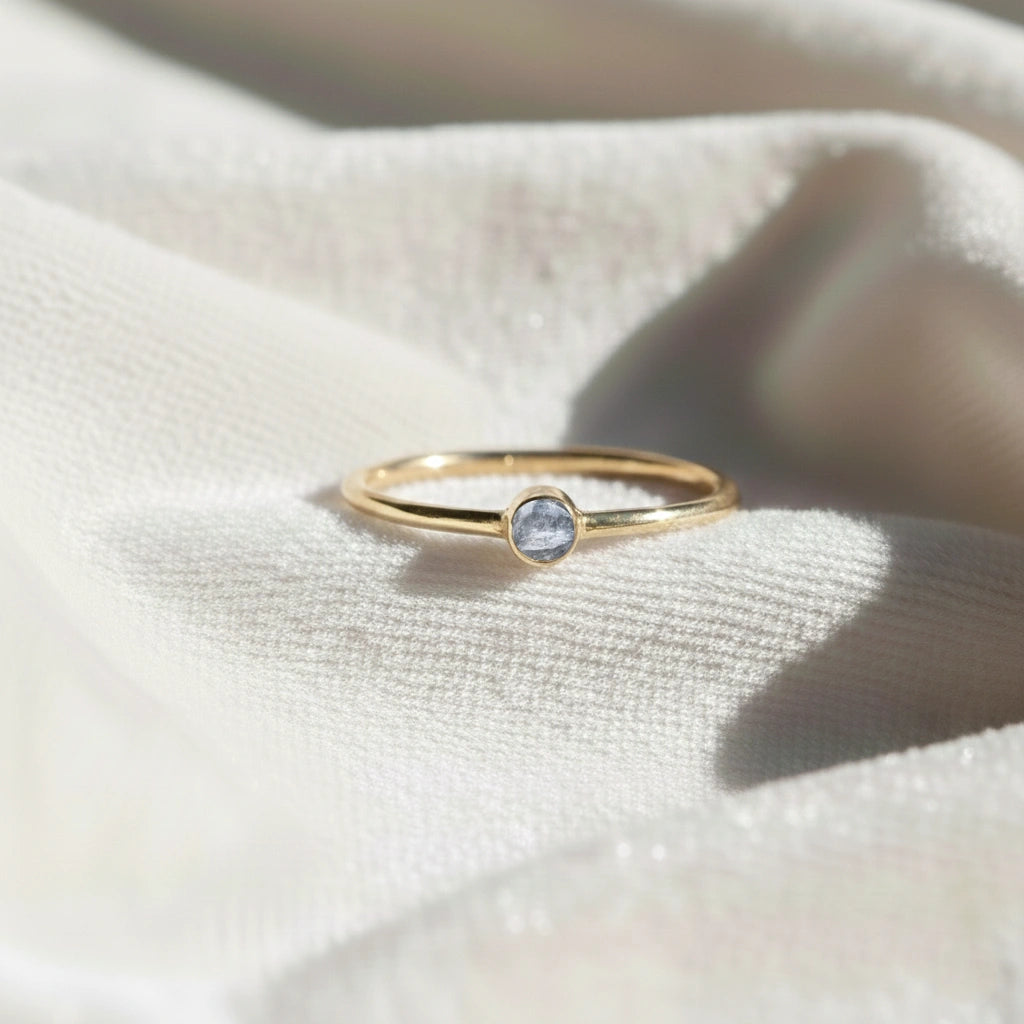 A gold plated birthstone ring featuring a clear quartz gemstone, styled as a delicate stacking ring on a soft white fabric background
