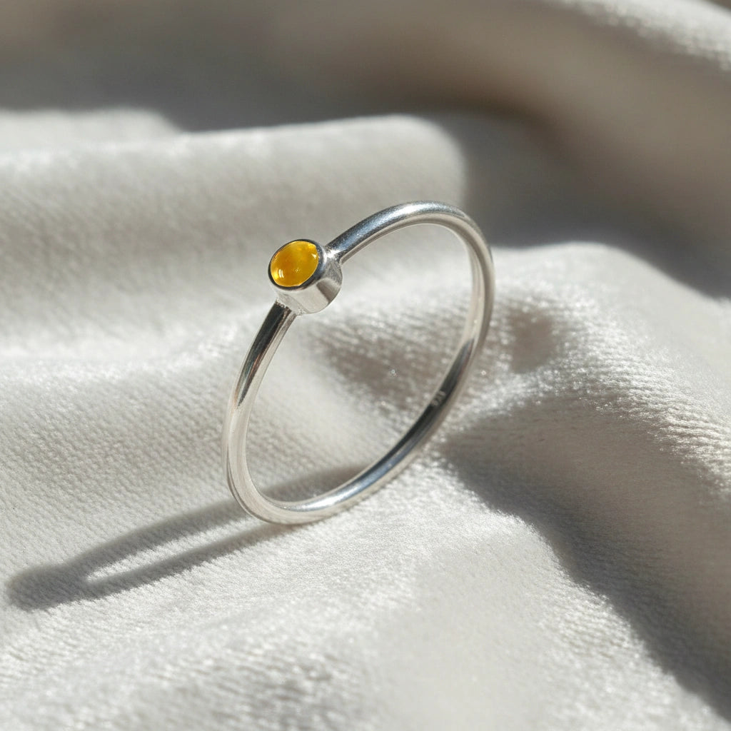 A silver birthstone ring featuring a citrine gemstone, styled as a delicate stacking ring on a soft white fabric background