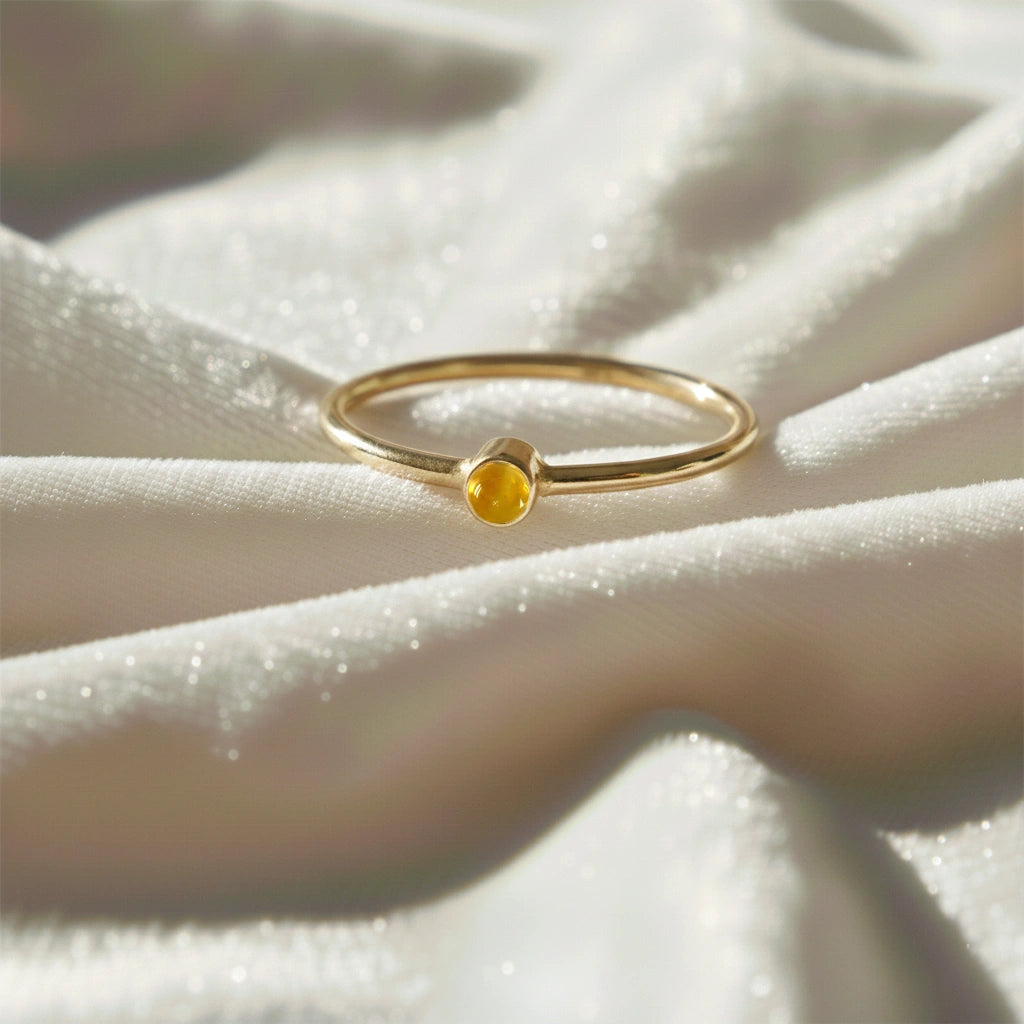 A gold plated birthstone ring featuring a citrine gemstone, styled as a delicate stacking ring on a soft white fabric background