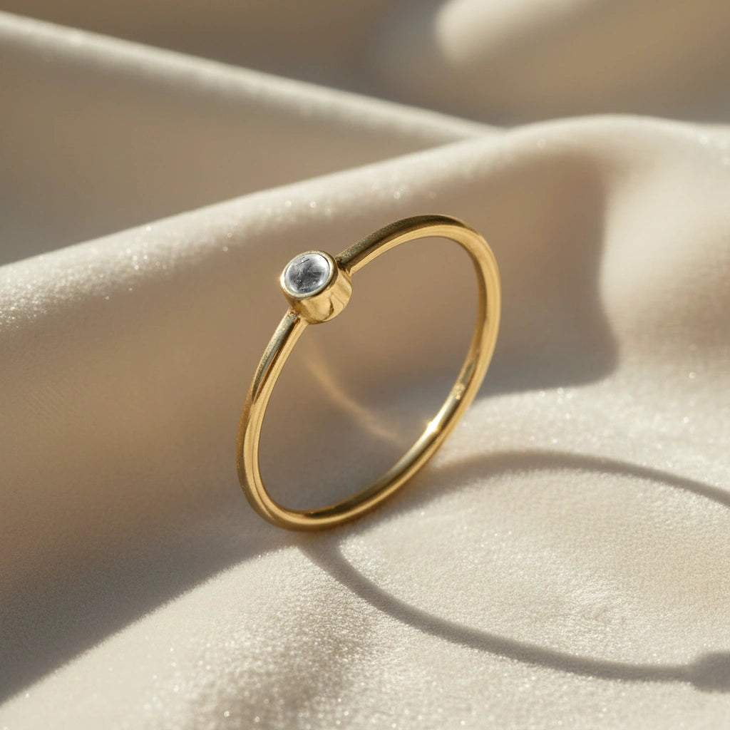 A gold plated birthstone ring featuring a white topaz gemstone, styled as a delicate stacking ring on a soft white fabric background