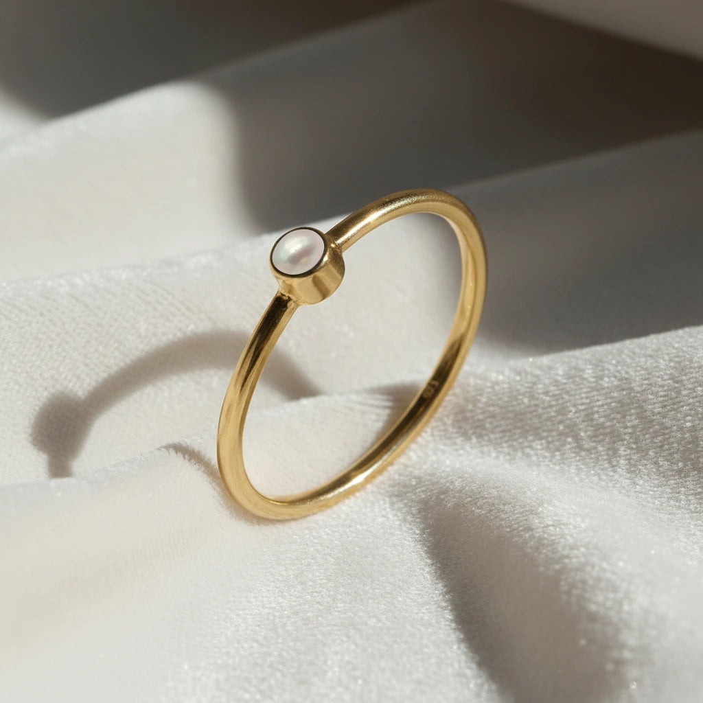 A gold plated birthstone ring featuring a pearl gemstone, styled as a delicate stacking ring on a soft white fabric background