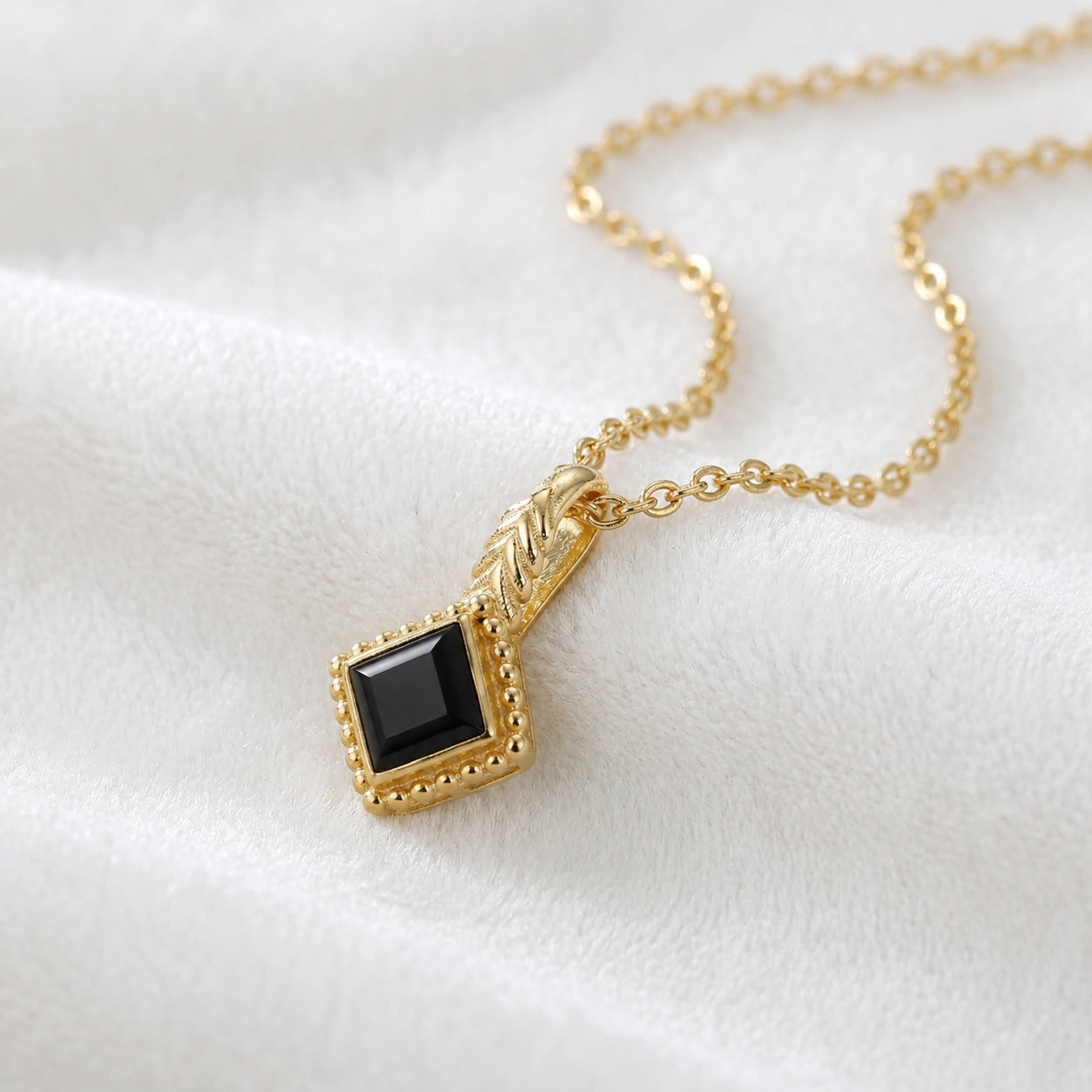 Birthstone_necklace_in_gold_plated_silver_with_square_cut_black_onyx_pendant_in_slightly_angled_view_on_soft_white_fabric_background