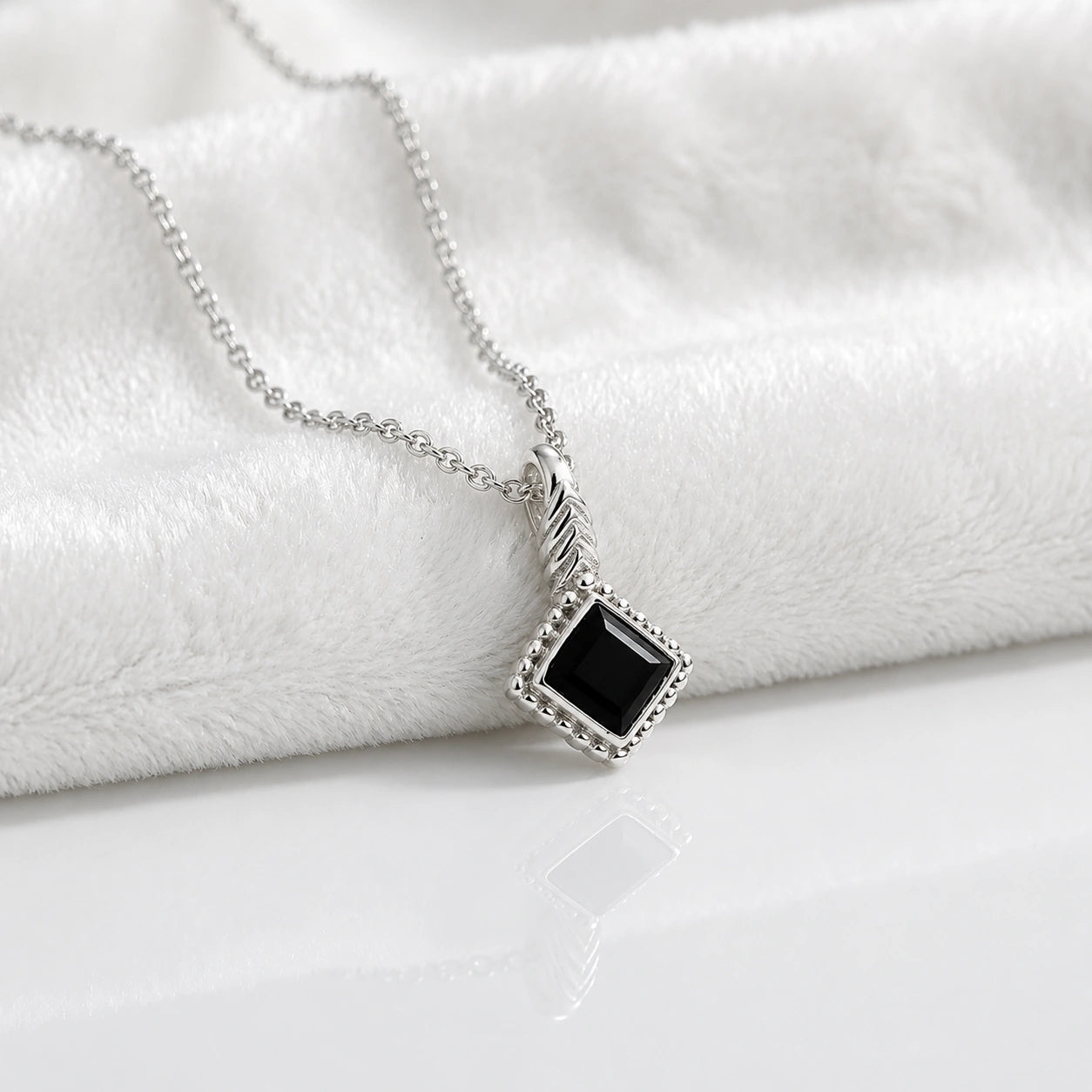Birthstone_necklace_in_sterling_silver_with_square_cut_black_onyx_pendant_in_slightly_angled_view_on_soft_white_fabric_background