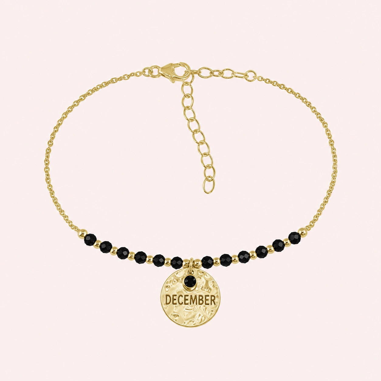 Birthstone_bracelet_in_gold_plated_silver_with_December_charm_and_black_onyx_beads_on_fine_chain_on_solid_pink_background
