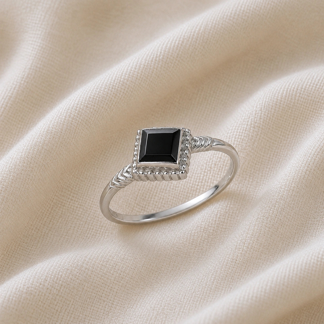 Princess_cut_ring_sterling_silver_with_square_black_onyx_and_detailed_band_slightly_tilted_view_on_soft_fabric_background