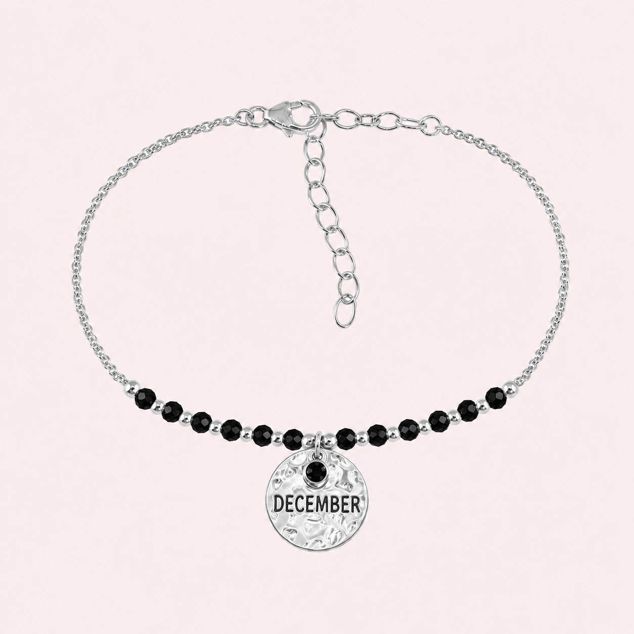 Birthstone_bracelet_in_sterling_silver_with_December_charm_and_black_onyx_beads_on_fine_chain_on_solid_pink_background