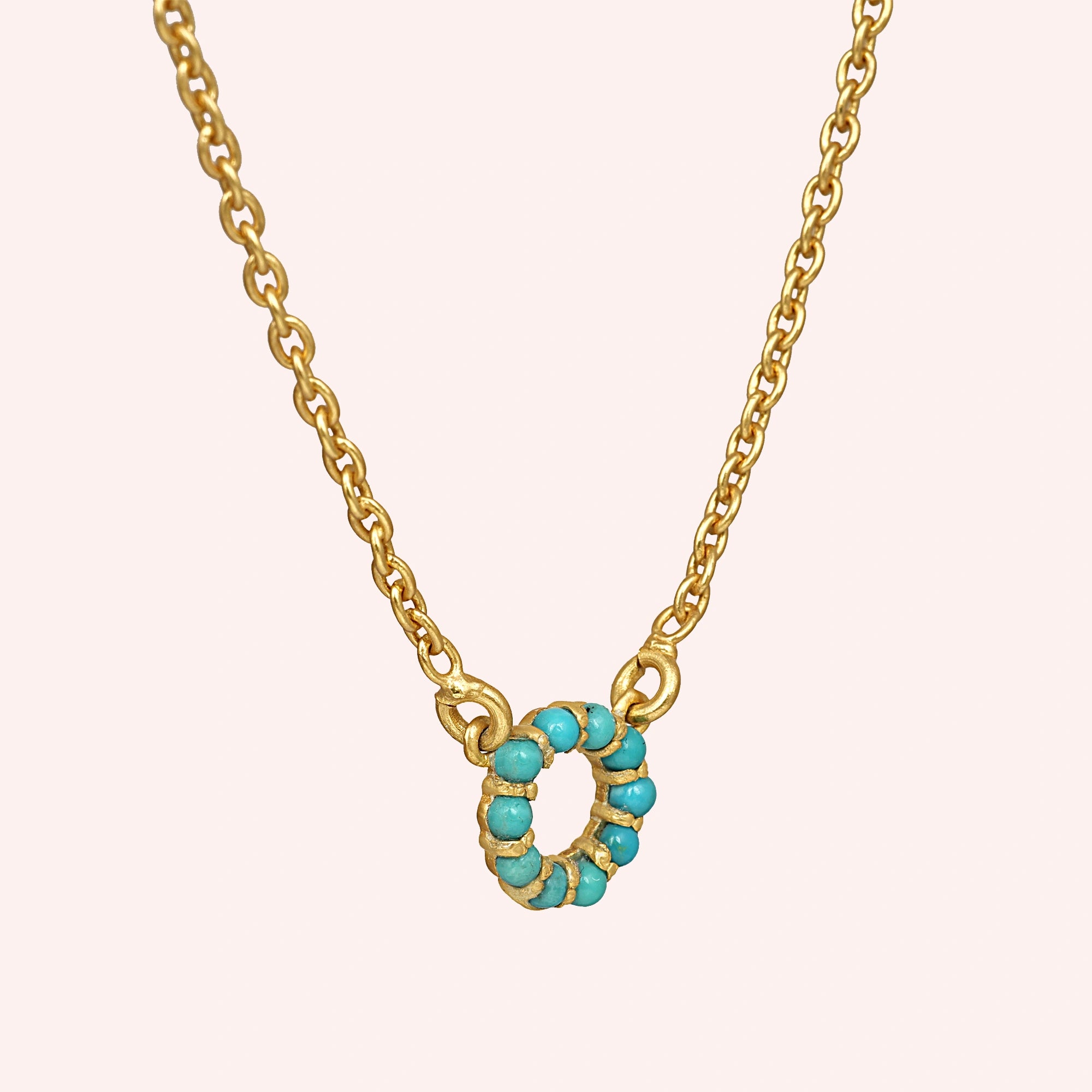 Blue_stone_necklace_in_gold_plated_silver_with_turquoise_stones_in_circle_pendant_at_slight_angle_view_on_solid_pink_background