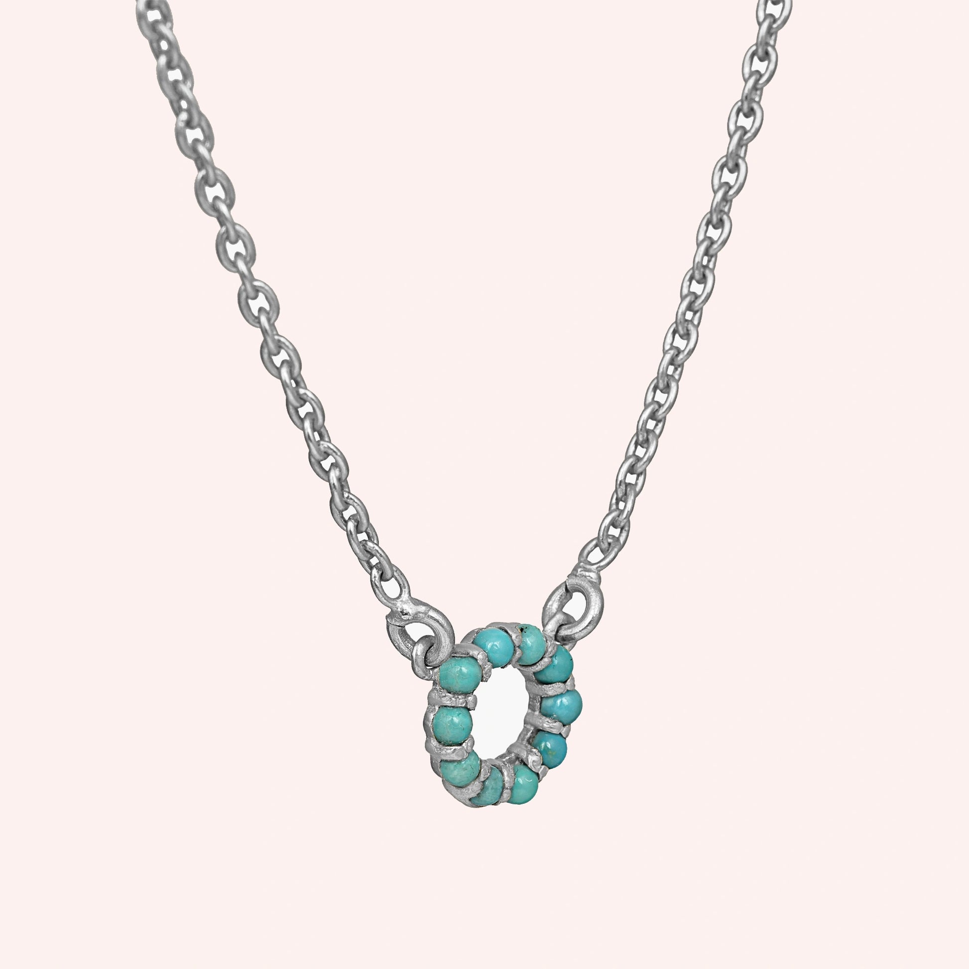 Blue_stone_necklace_in_sterling_silver_with_turquoise_stones_in_circle_pendant_at_slight_angle_view_on_solid_pink_background