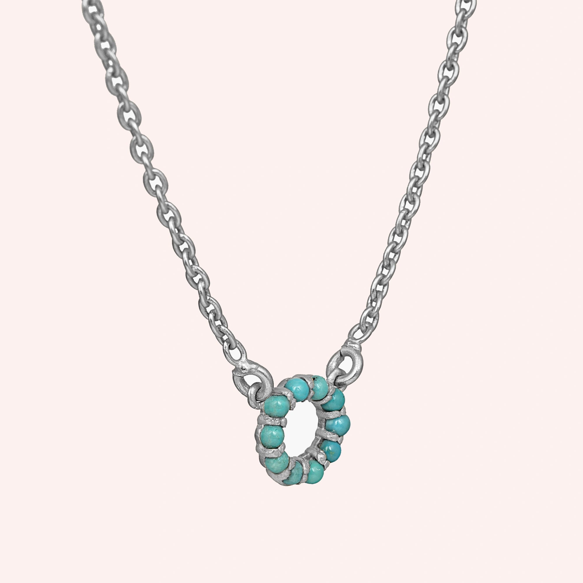 Blue_stone_necklace_in_sterling_silver_with_turquoise_stones_in_circle_pendant_at_slight_angle_view_on_solid_pink_background