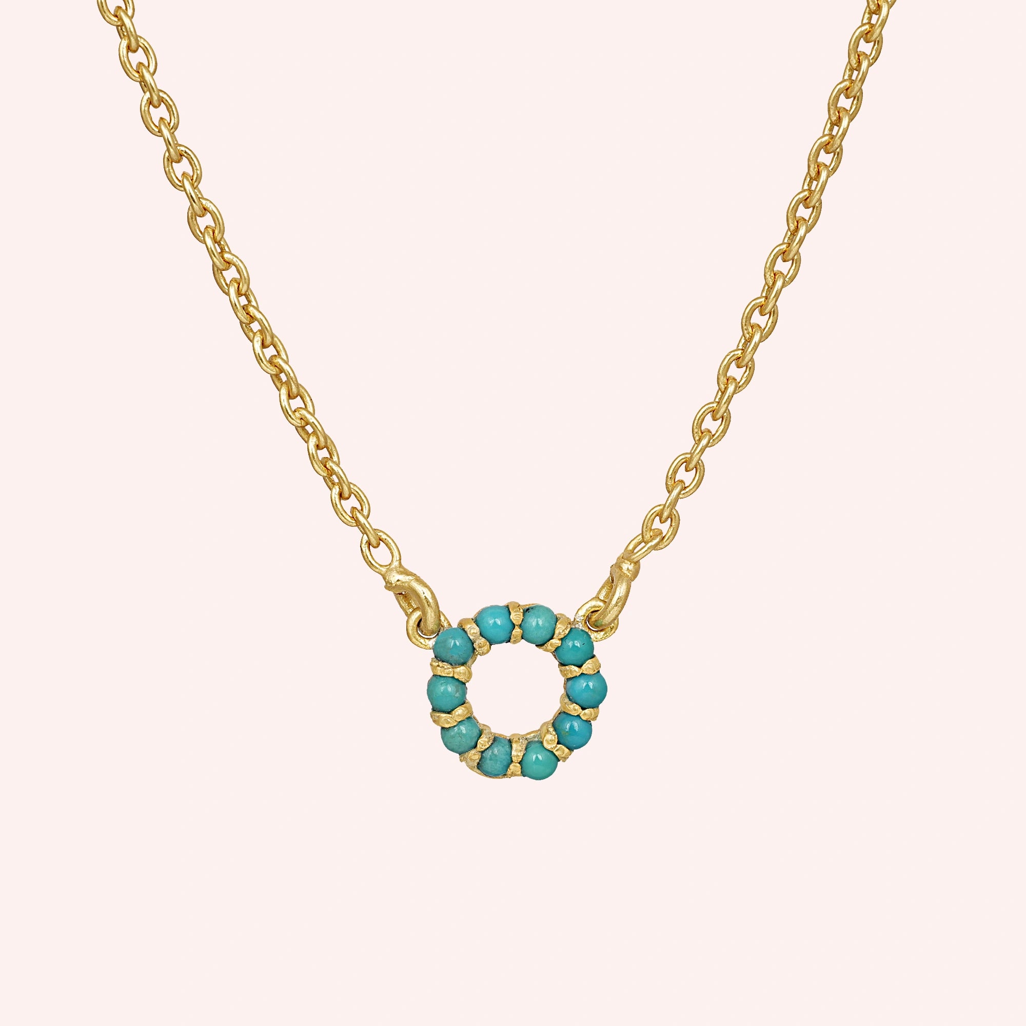 Blue_stone_necklace_in_gold_plated_silver_with_turquoise_stones_in_circle_pendant_at_front_angle_view_on_solid_pink_background
