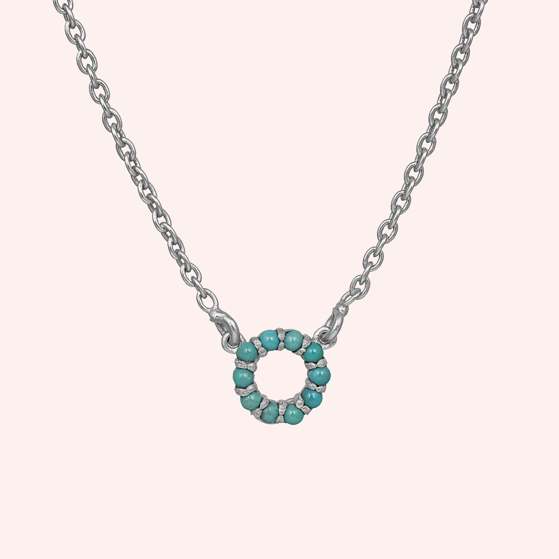 Blue_stone_necklace_in_sterling_silver_with_turquoise_stones_in_circle_pendant_at_front_angle_view_on_solid_pink_background