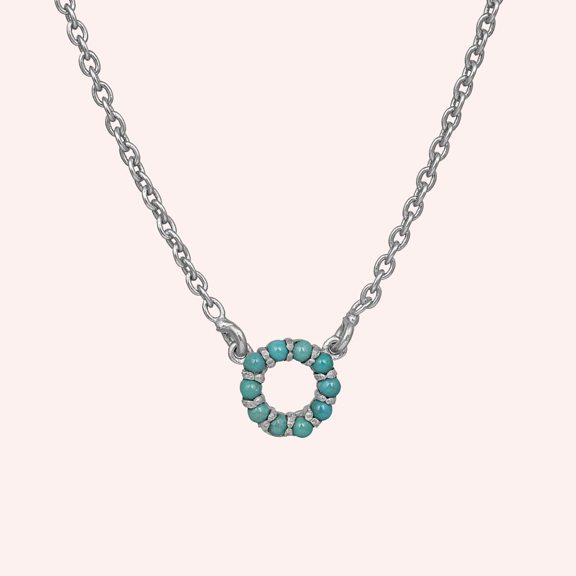 Blue_stone_necklace_in_sterling_silver_with_turquoise_stones_in_circle_pendant_at_front_angle_view_on_solid_pink_background