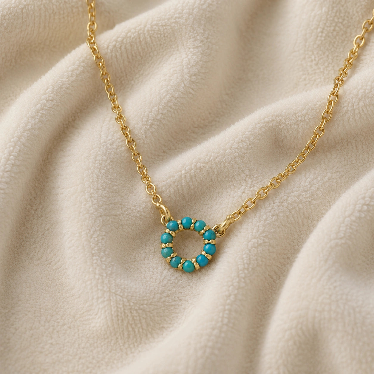 Blue_stone_necklace_in_gold_plated_silver_with_turquoise_stones_in_circle_pendant_at_slight_angle_view_on_soft_fabric_background