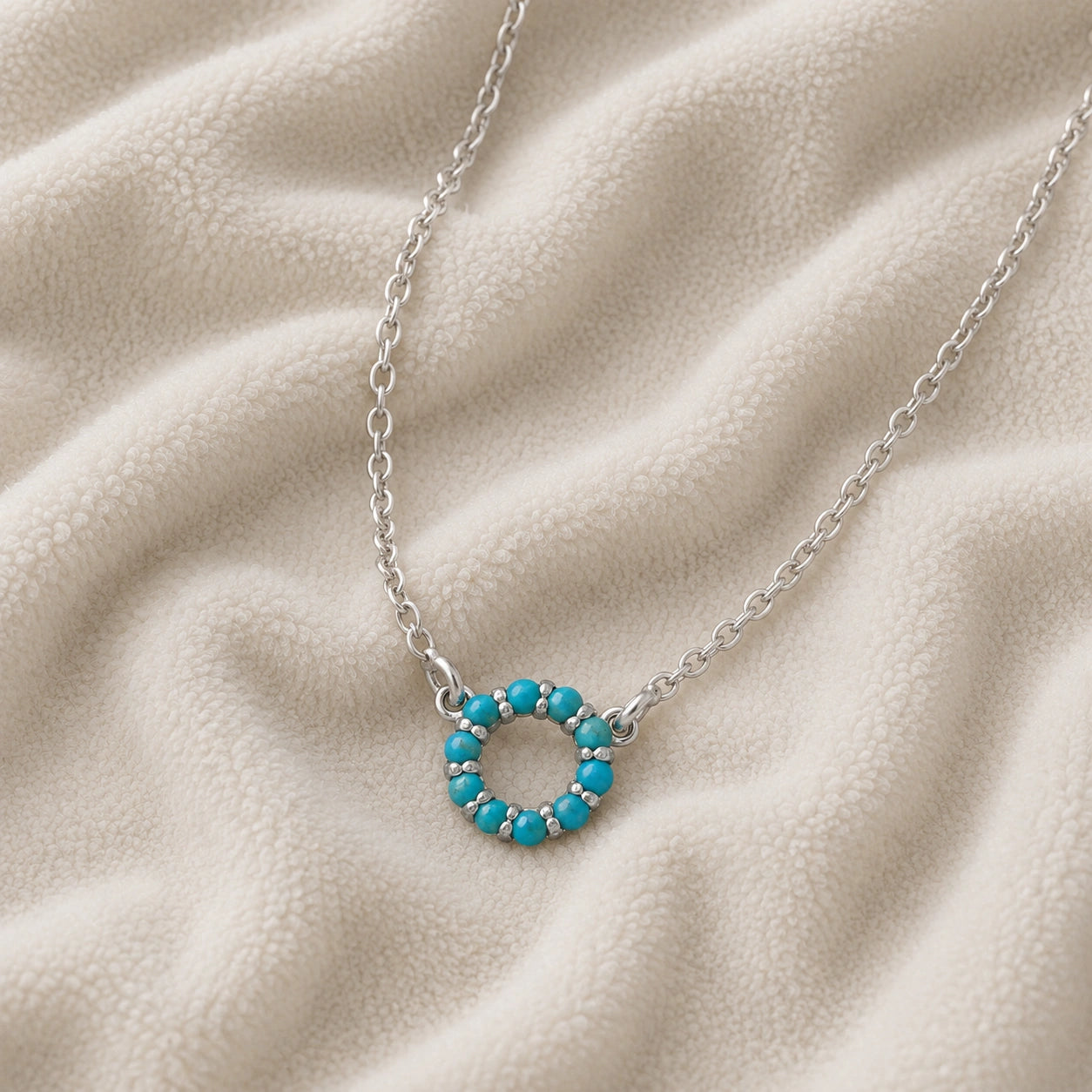 Blue_stone_necklace_in_sterling_silver_with_turquoise_stones_in_circle_pendant_at_slight_angle_view_on_soft_fabric_background