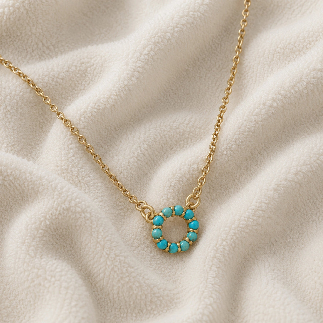 Blue_stone_necklace_in_gold_plated_silver_with_turquoise_stones_in_circle_pendant_at_front_angle_view_on_soft_fabric_background