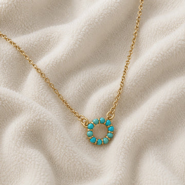 Blue_stone_necklace_in_gold_plated_silver_with_turquoise_stones_in_circle_pendant_at_front_angle_view_on_soft_fabric_background