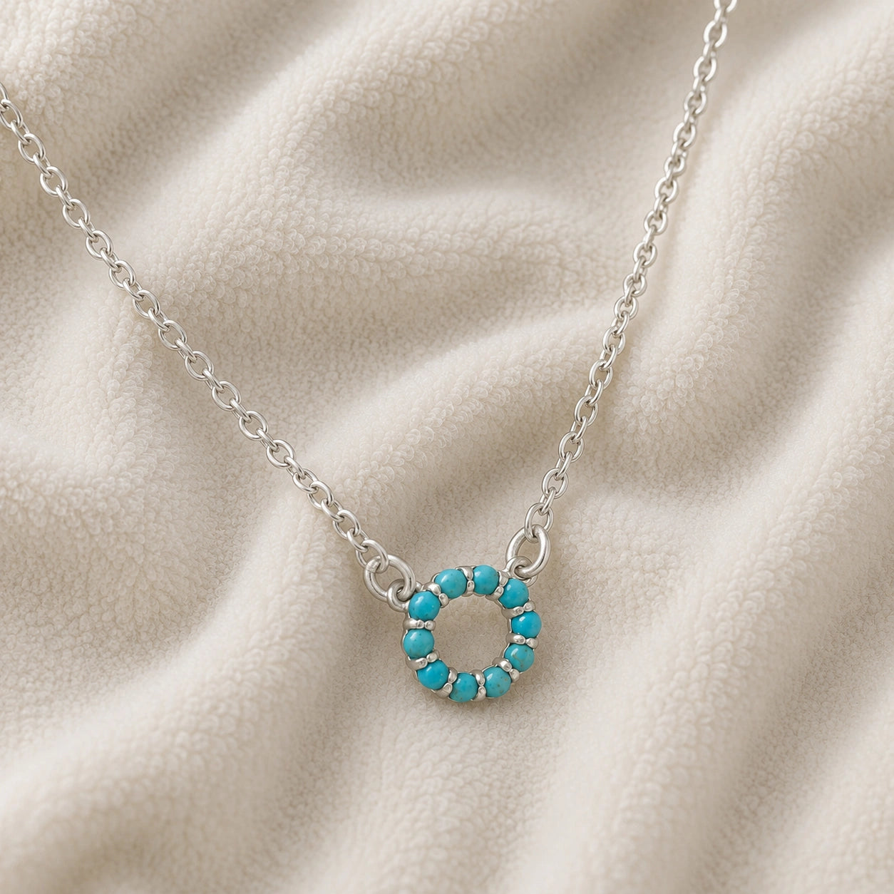Blue_stone_necklace_in_sterling_silver_with_turquoise_stones_in_circle_pendant_at_front_angle_view_on_soft_fabric_background