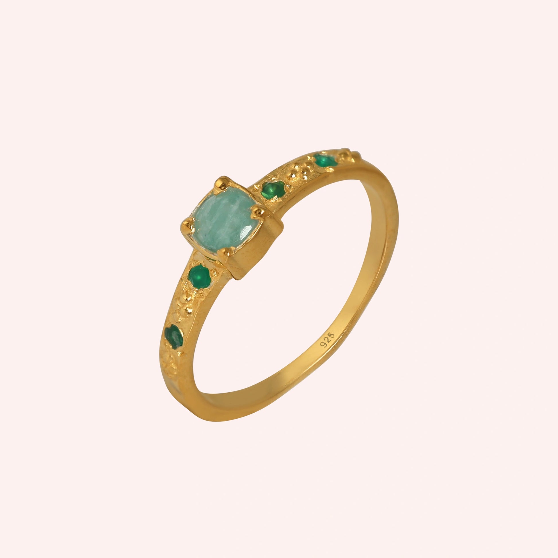 Blue-stone-ring-in-gold-plated-silver-with-green-stones-in-angled-side-view-on-solid-pink-background