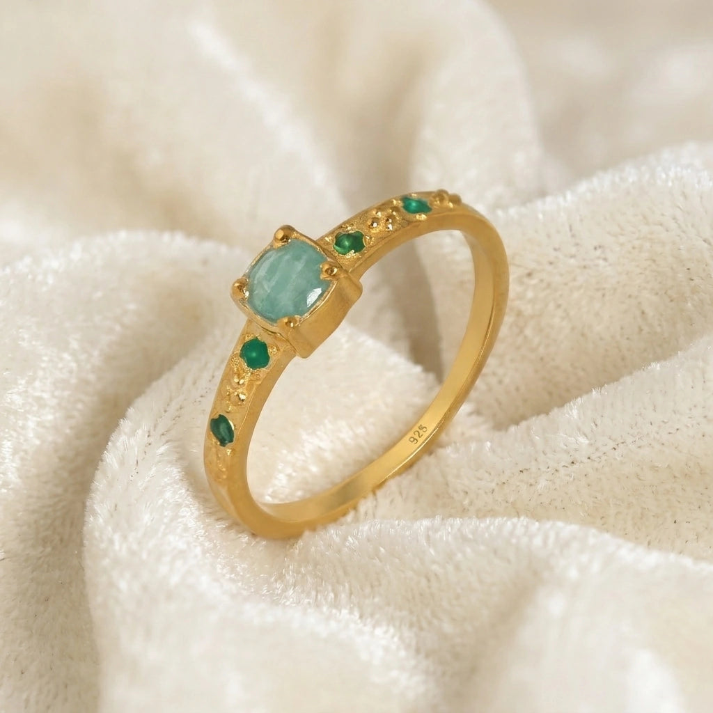 Blue-stone-ring-in-gold-plated-silver-with-green-stones-in-angled-side-view-on-soft-cream-fabric-background