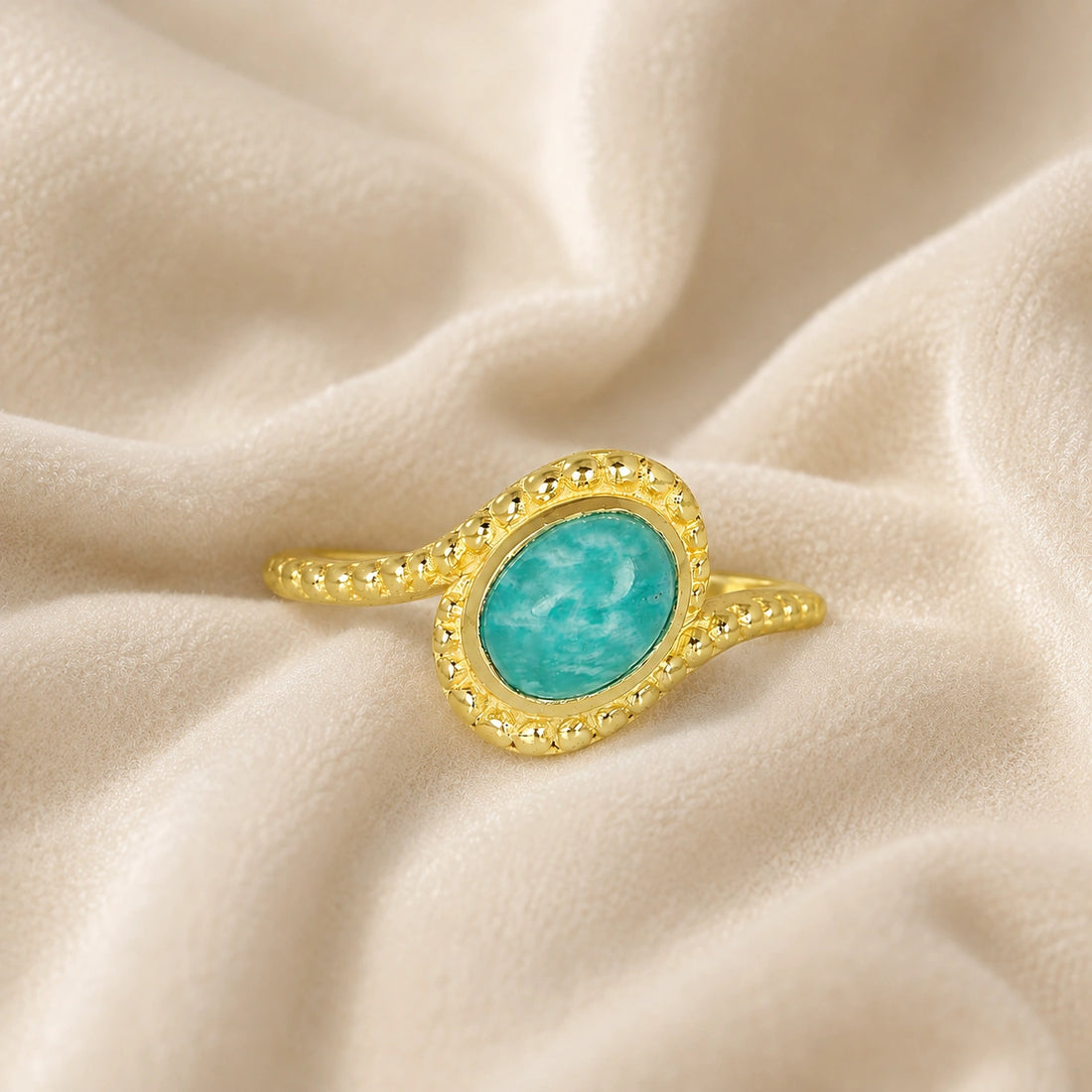 Blue_stone_ring_in_gold_plated_silver_with_an_oval_amazonite_stone_at_front_angle_view_on_soft_fabric_background
