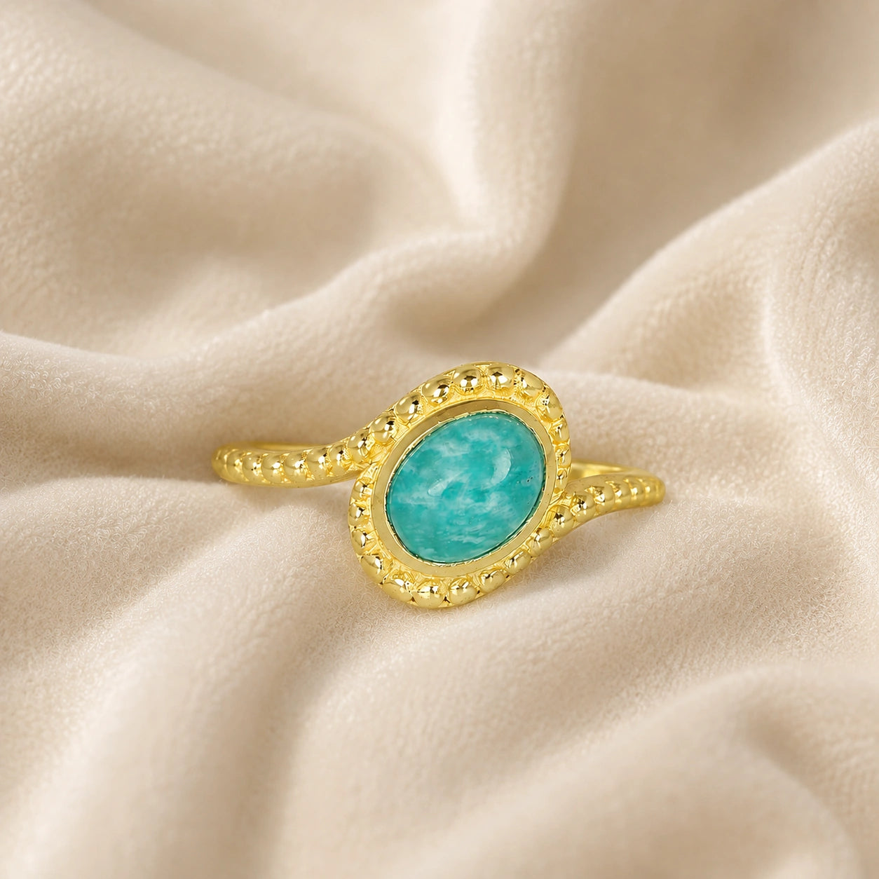 Blue_stone_ring_in_gold_plated_silver_with_an_oval_amazonite_stone_at_front_angle_view_on_soft_fabric_background