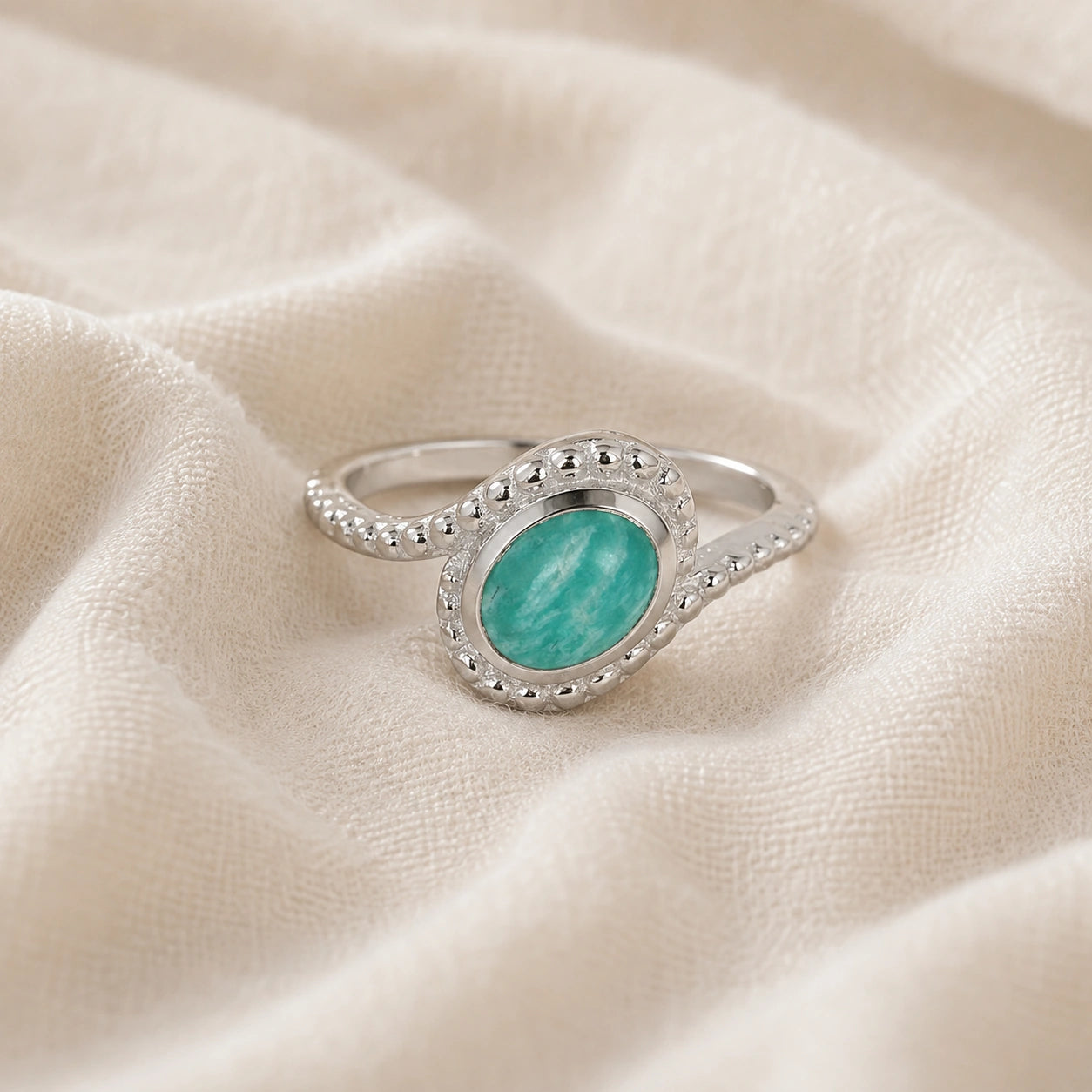 Blue_stone_ring_in_sterling_silver_with_an_oval_amazonite_stone_at_front_angle_view_on_soft_fabric_background
