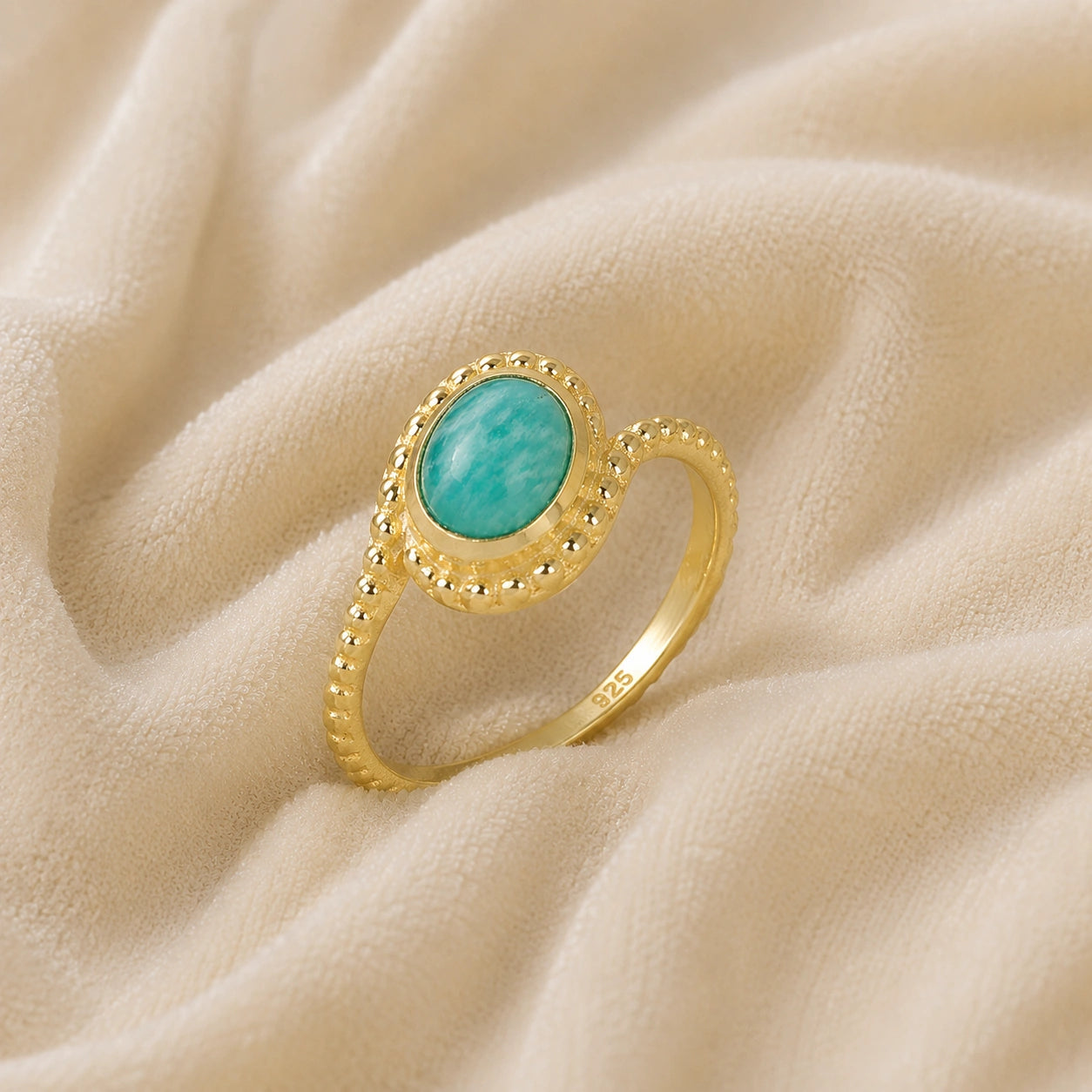 Blue_stone_ring_in_gold_plated_silver_with_an_oval_amazonite_stone_at_slight_angle_view_on_soft_fabric_background