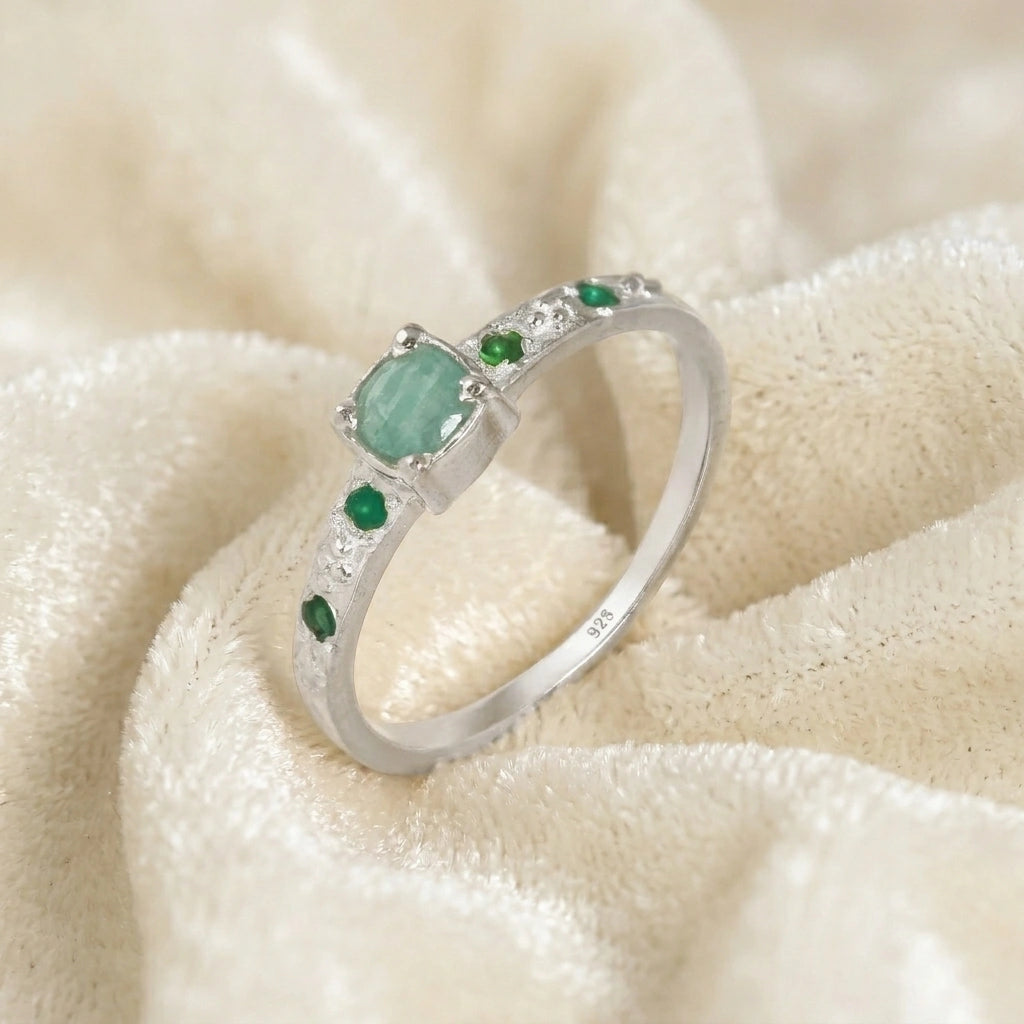Blue-stone-ring-in-sterling-silver-with-green-stones-in-angled-side-view-on-soft-cream-fabric-background