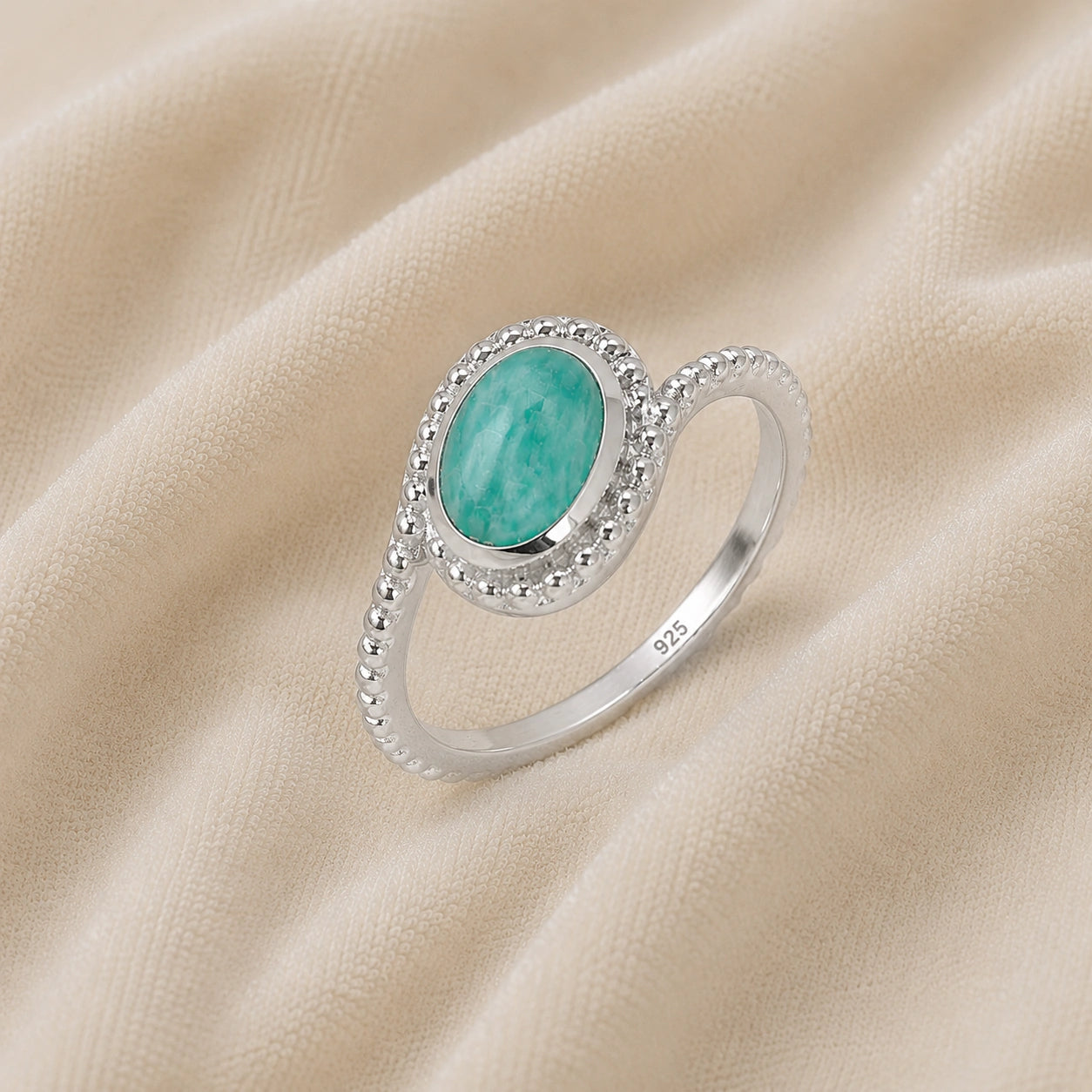 Blue_stone_ring_in_sterling_silver_with_an_oval_amazonite_stone_at_slight_angle_view_on_soft_fabric_background