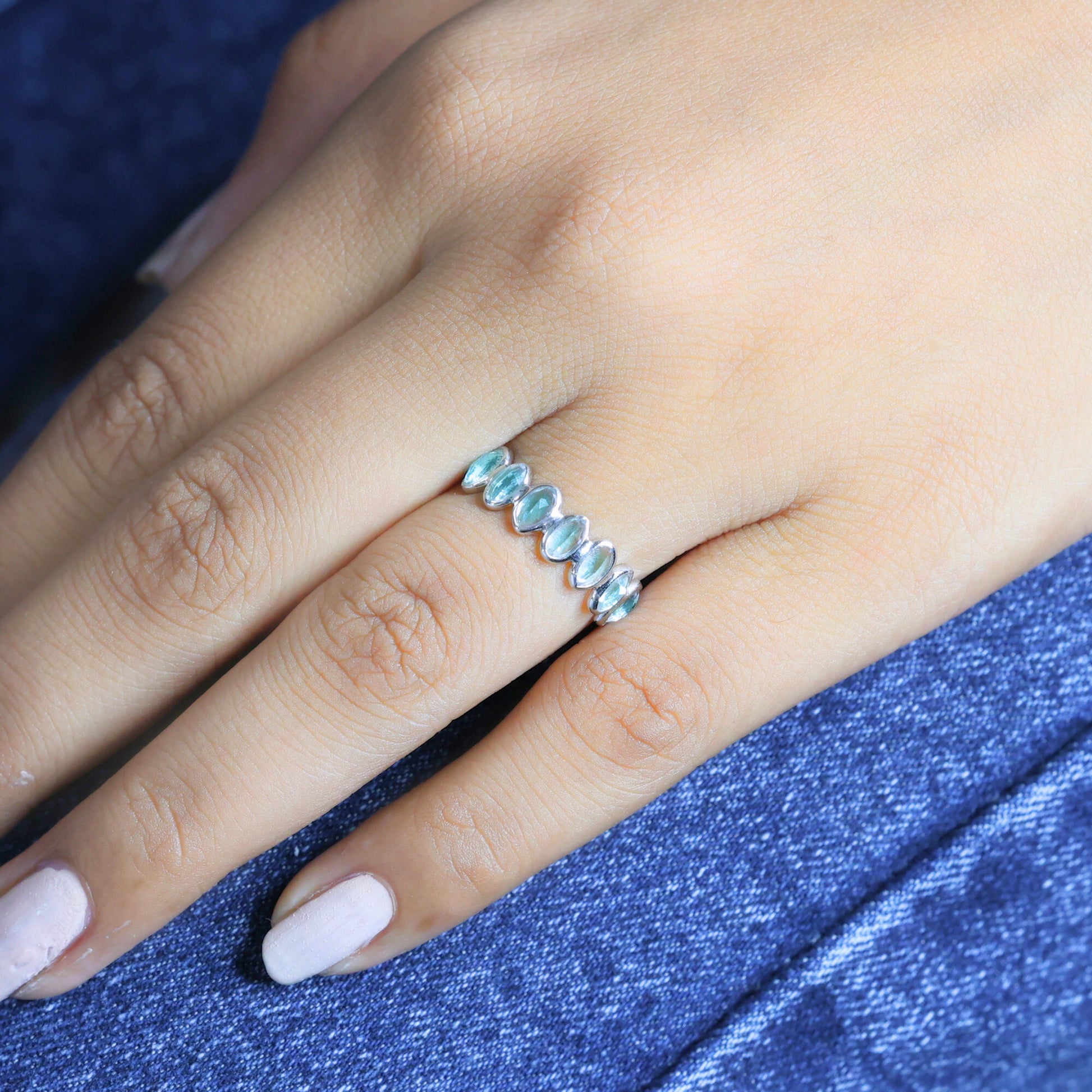 Sterling silver topaz ring featuring light blue oval gems on a woman's finger resting on blue jeans angled close-up view.