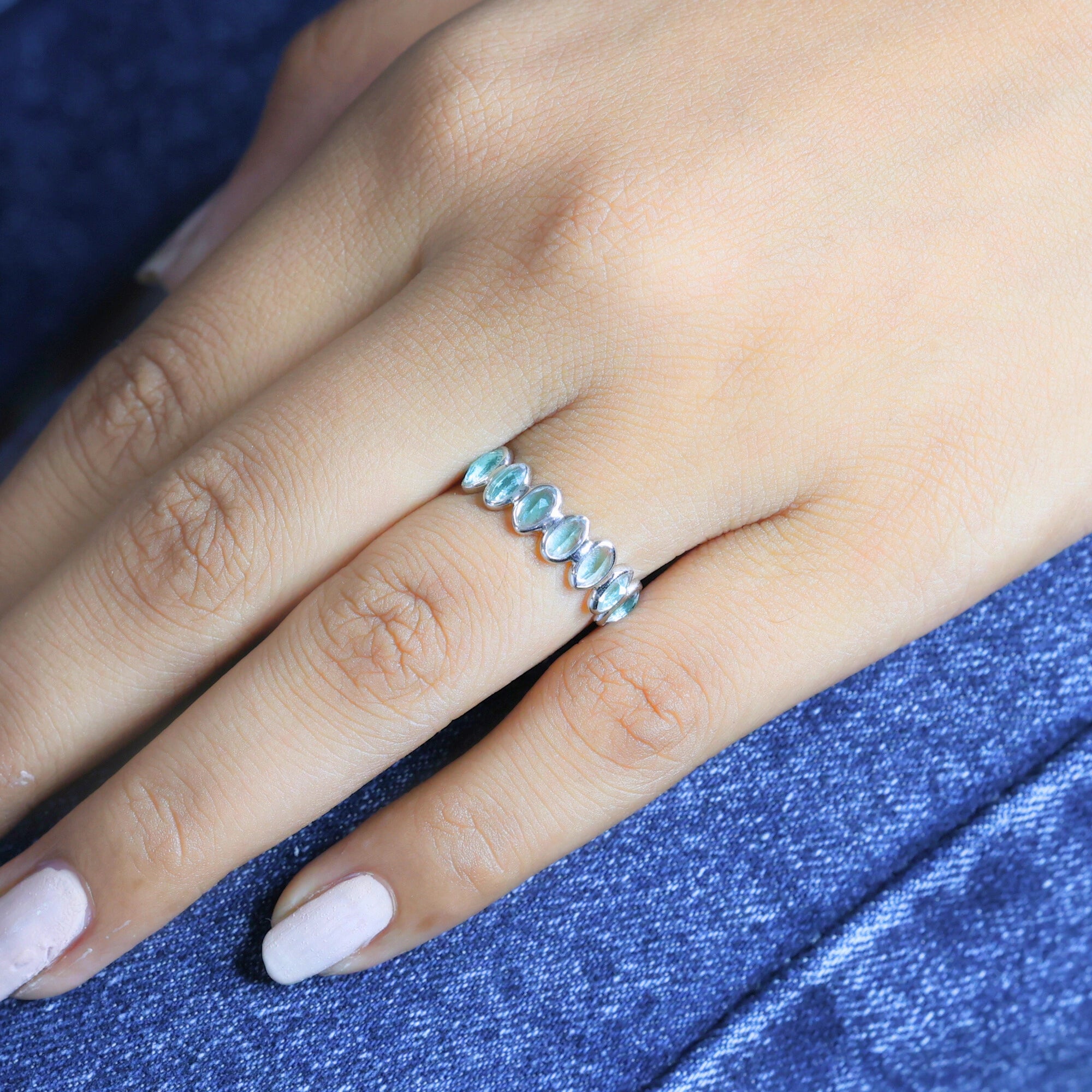 Sterling silver topaz ring featuring light blue oval gems on a woman's finger resting on blue jeans angled close-up view.