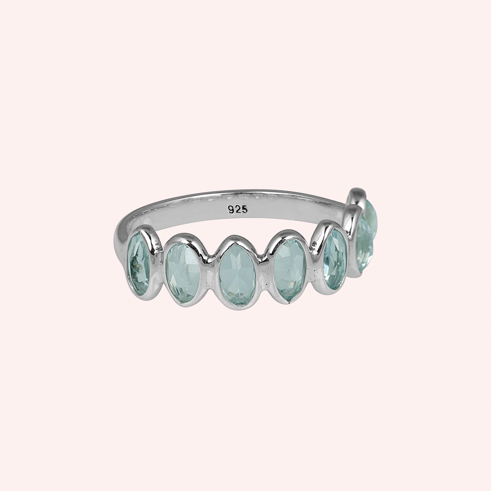 Sterling silver topaz ring featuring seven oval light blue gemstones on a plain pink background front view.