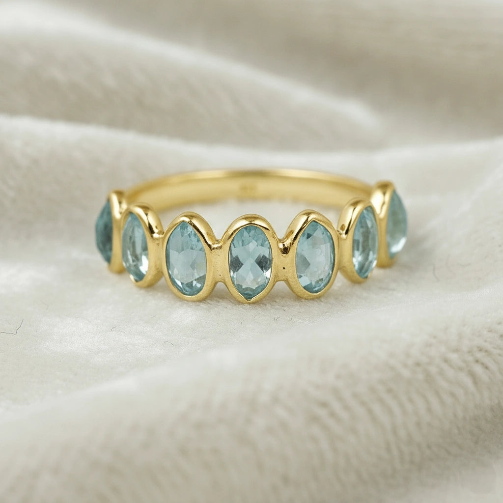 Sterling silver topaz ring band featuring light blue oval gems resting on a white velvet fabric close-up perspective.