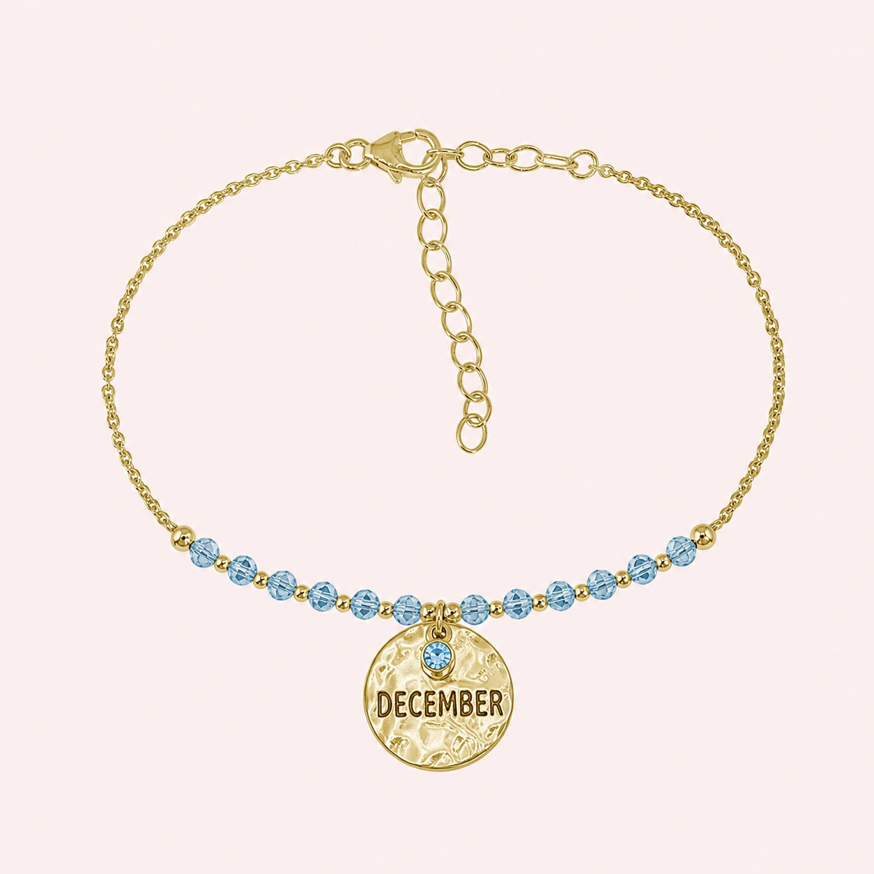 Birthstone_bracelet_in_gold_plated_silver_with_December_charm_and_blue_topaz_beads_on_fine_chain_on_solid_pink_background