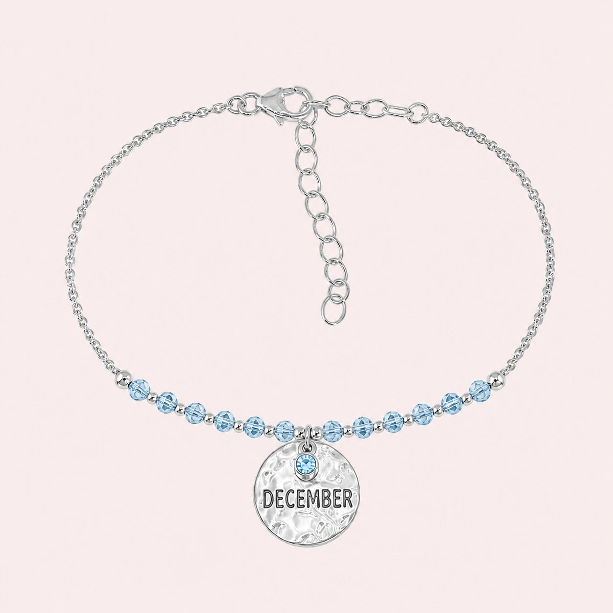 Birthstone_bracelet_in_sterling_silver_with_December_charm_and_blue_topaz_beads_on_fine_chain_on_solid_pink_background