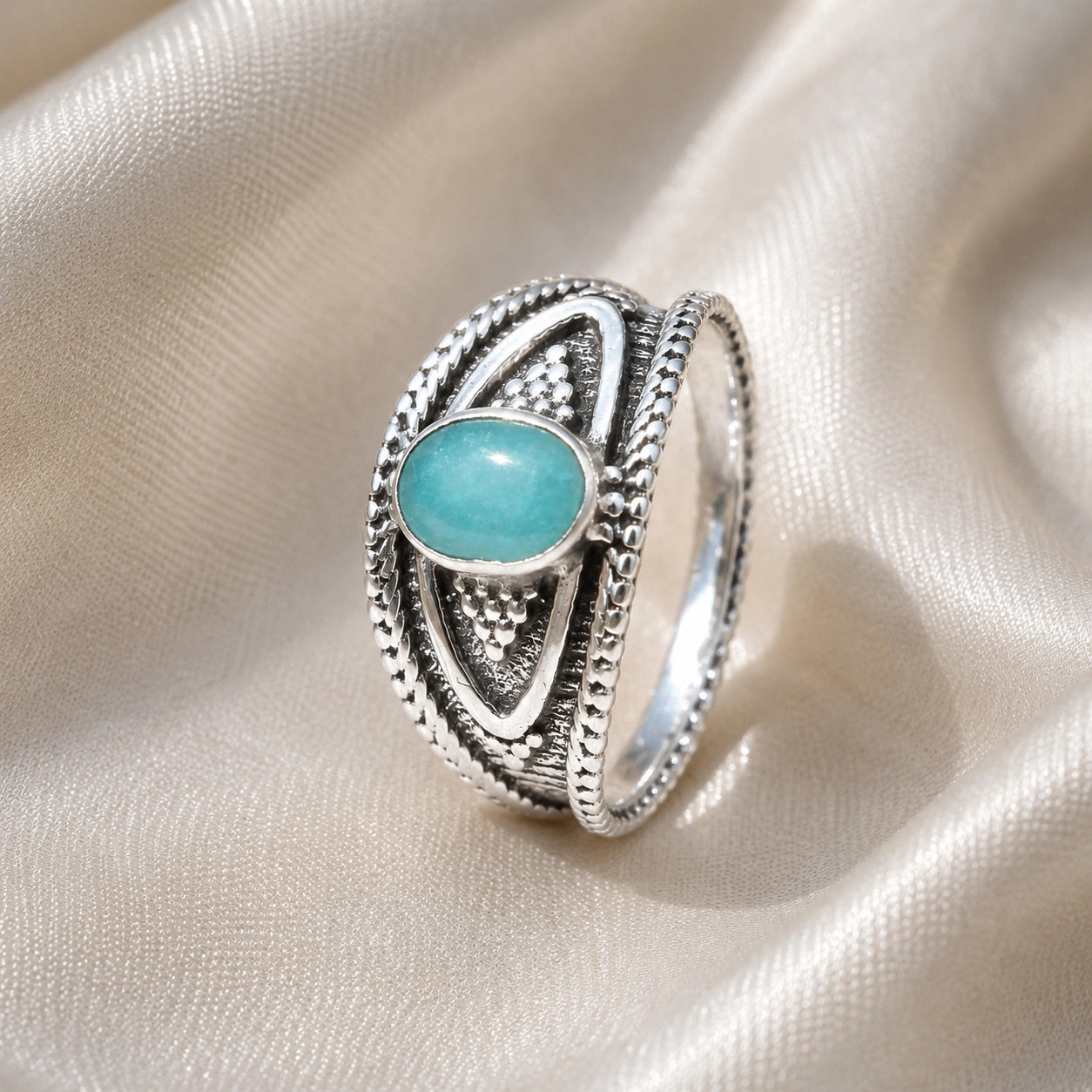 Boho_ring_with_amazonite_stone_sterling_silver_with_filigree_texture_in_slightly_angled_on_soft_fabric_background