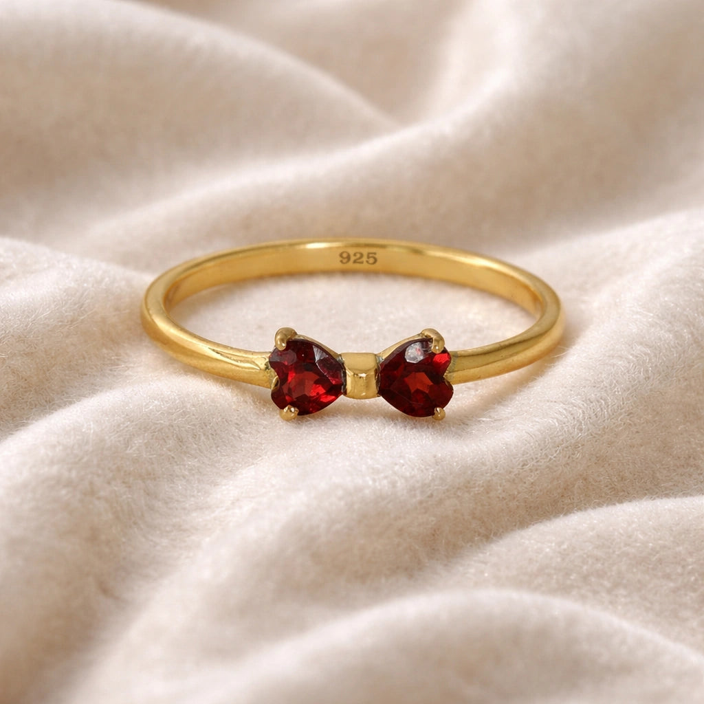 Bow_ring_close_up_front_angle_shot_gold_plated_silver_band_red_heart_garnet_gemstones_on_soft_off_white_fabric_background