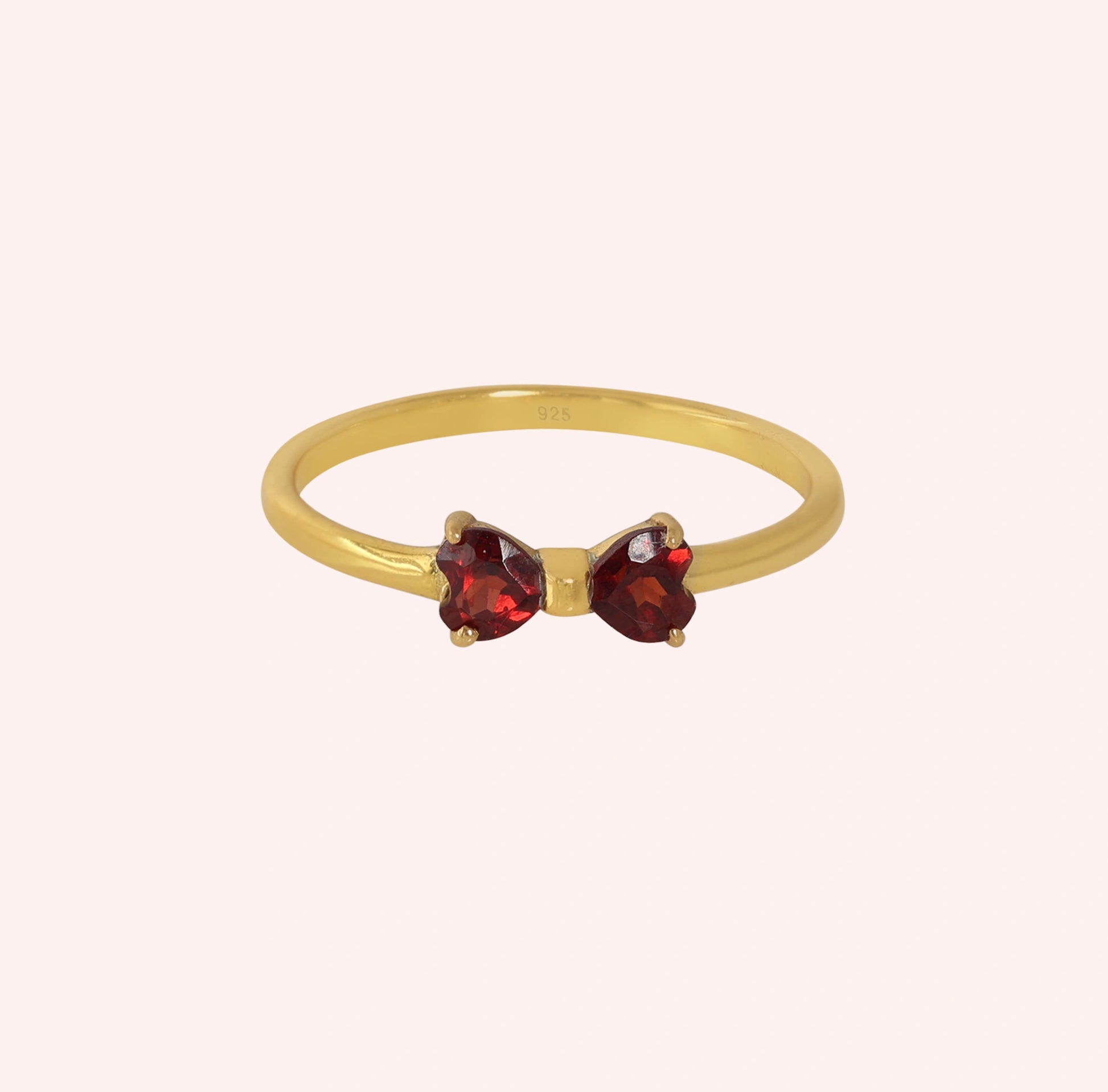 Bow_ring_close_up_front_angle_shot_gold_plated_silver_band_red_heart_garnet_gemstones_on_solid_pink_background